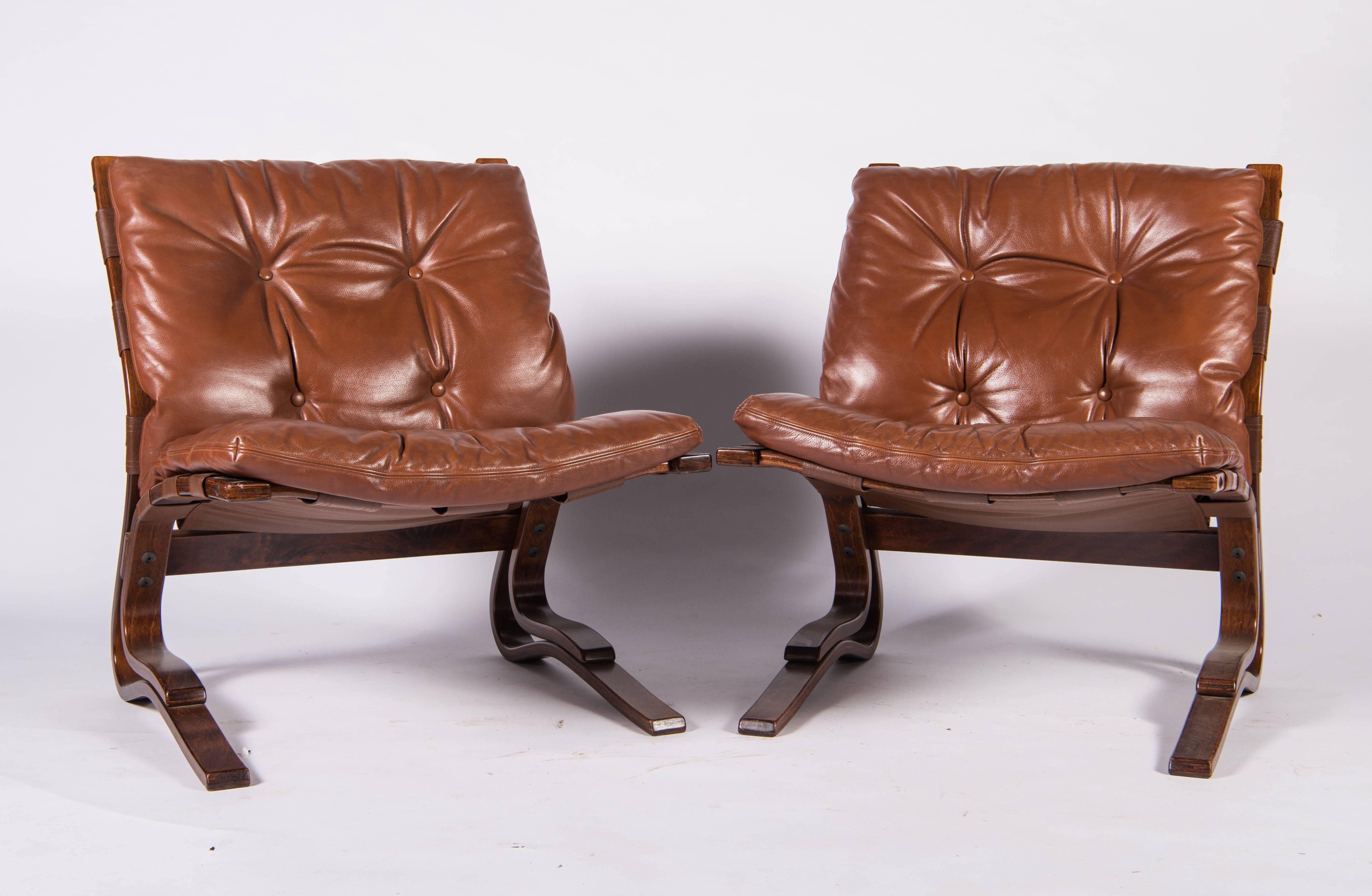 A pair of iconic cantilevered chairs of bent laminated rosewood with cushions of tufted brown leather by Elsa and Nordahl Solheim for Rykkin & Company of Norway. . The gentle 'flex' of the chair makes them exceedingly comfortable and their clean,