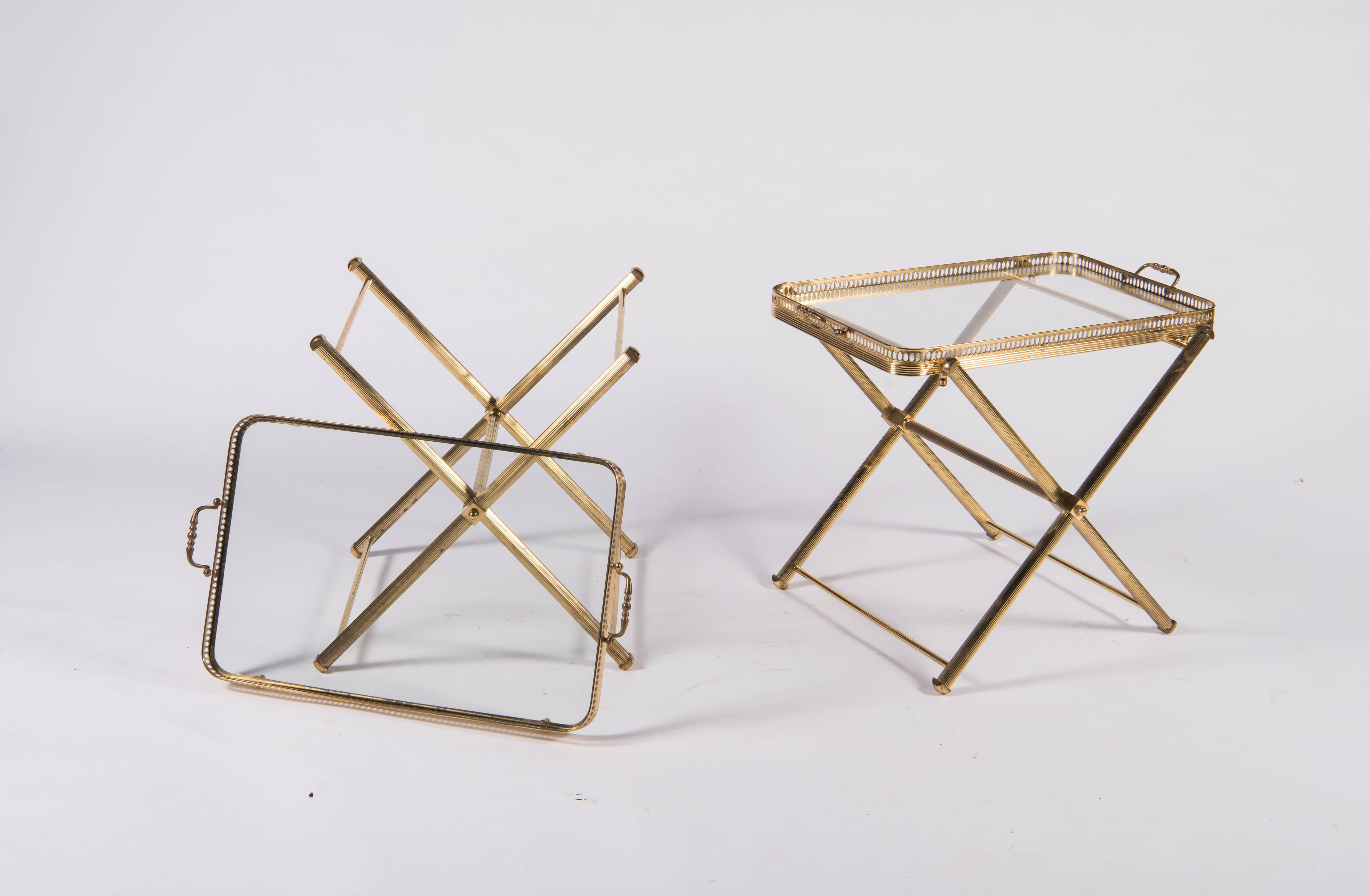 A pair of brass and glass tray tables that fold for easy storage. The frame of channeled tubular brass holds a footed tray with handles. The tray is 14.5 inches x 21 inches with a 1 inch deep brass filigreed gallery surrounding an insert of