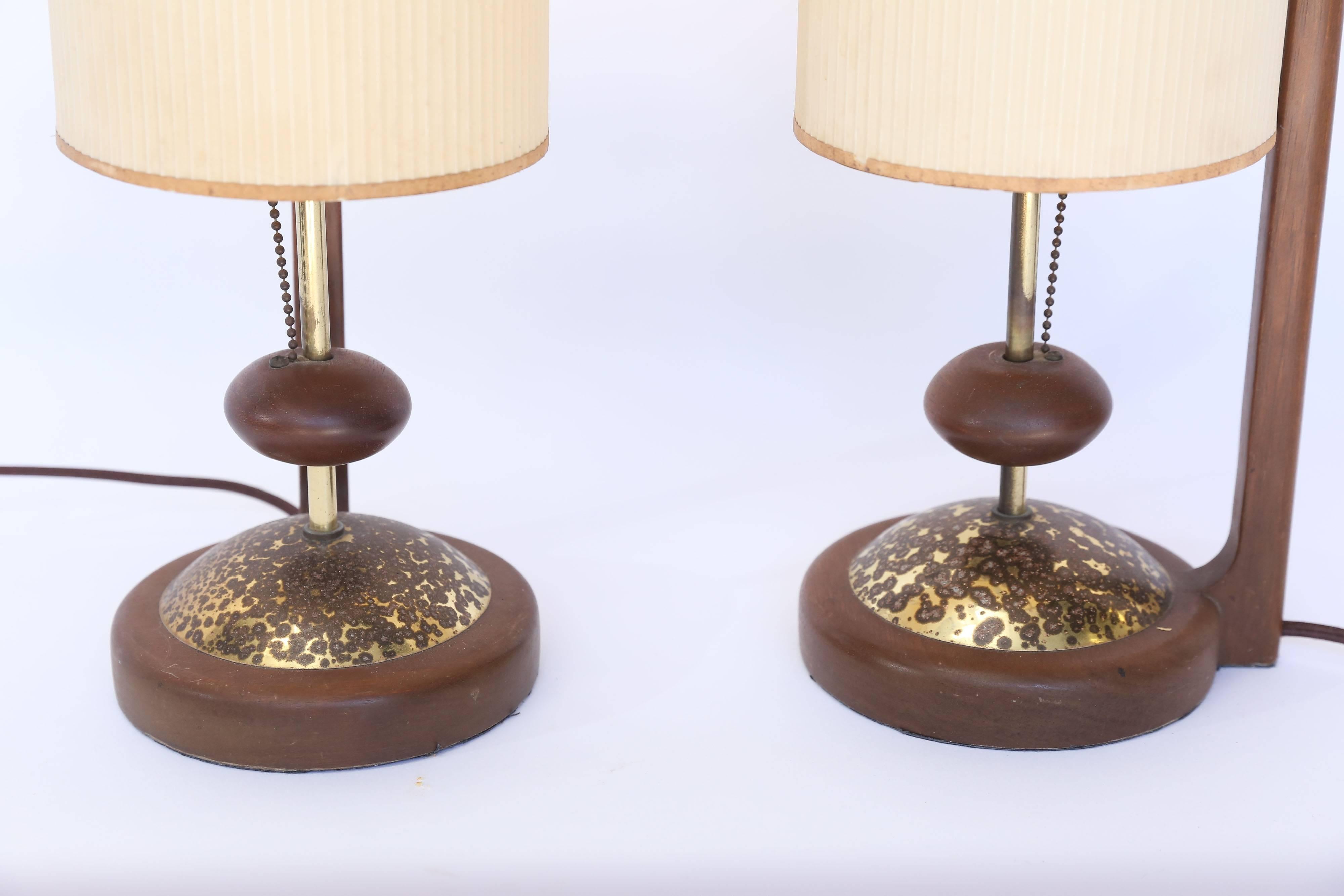 A pair of Mid-Century Danish teak table lamps in near perfect condition. The base is accented in brass with a fired patina. The shades are ribbed fiberglass attached to a teak spire. The chain pull is connected to teak knobs on the stem of the lamp.