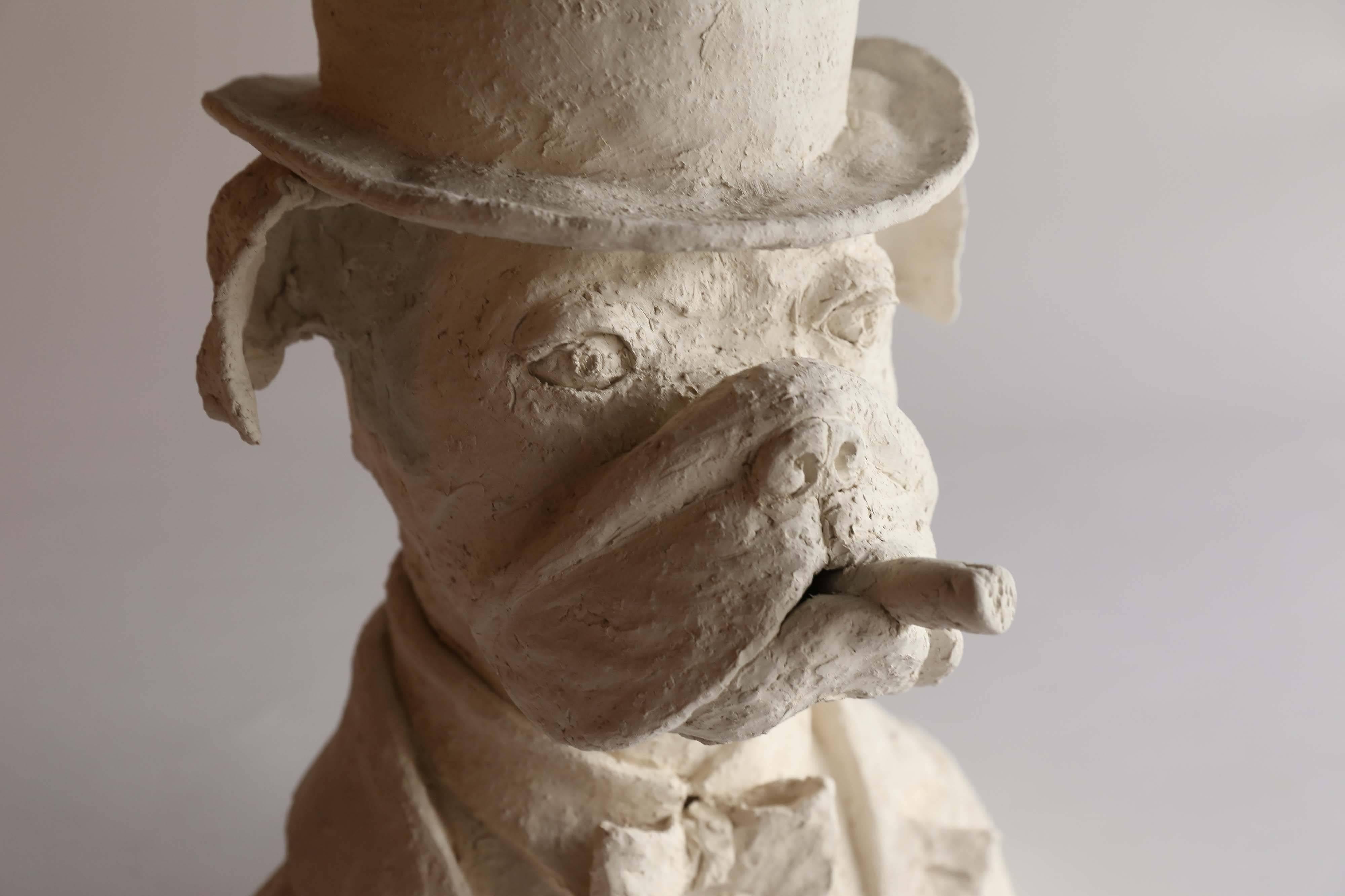 A plaster bust of a dapper bulldog. With his jaunty hat and bow tie, this dignified fellow exudes a businesslike air of confidence as he smokes his stogie. From France, the bust is signed LL.
