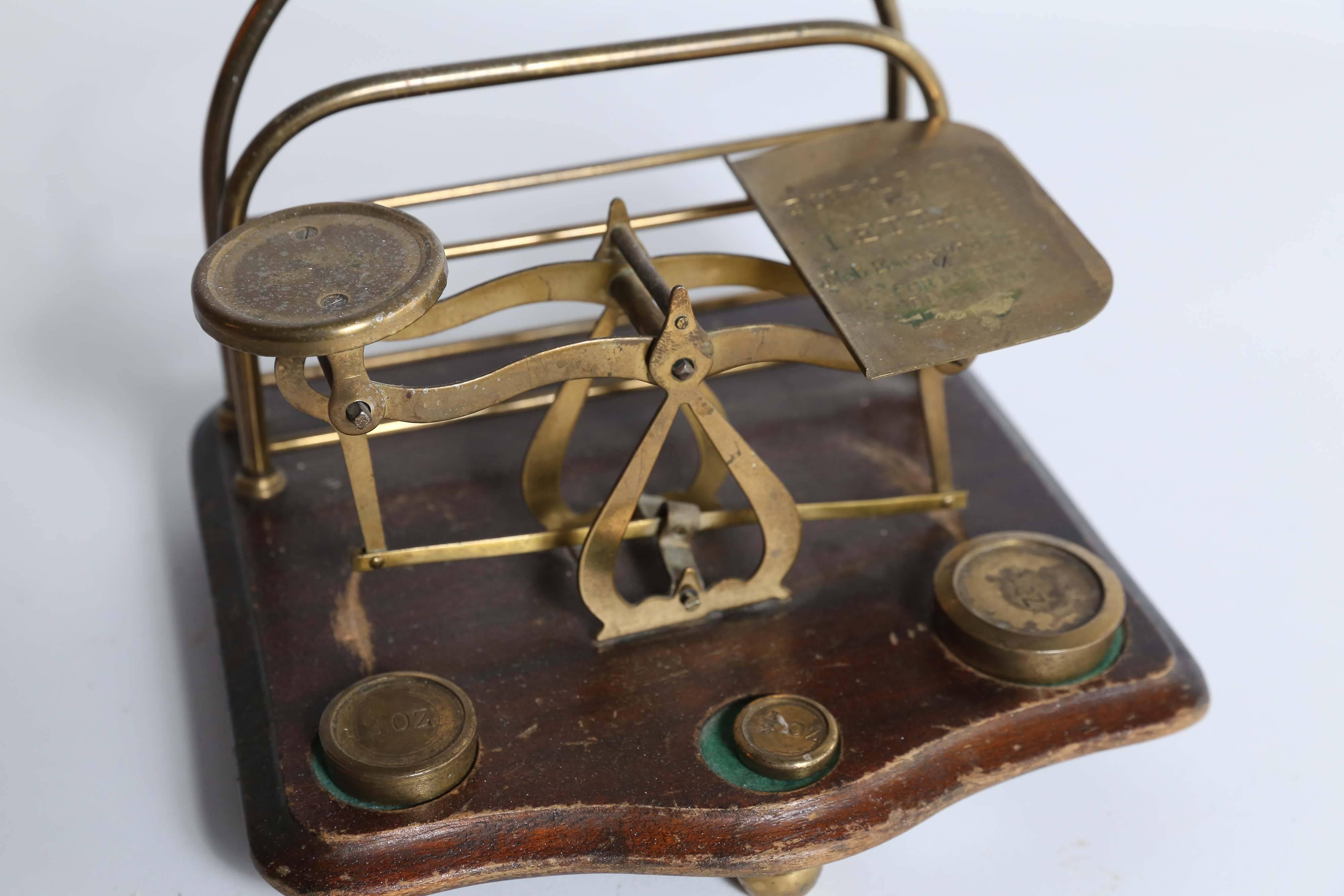 A mahogany and brass postage scale found in France but most likely British. Standing on three brass ball feet, the scale comes with three brass weights, 1/2 oz, 2 oz, and 4 oz, each of which rest in a recessed and felted slot. With a serpentine