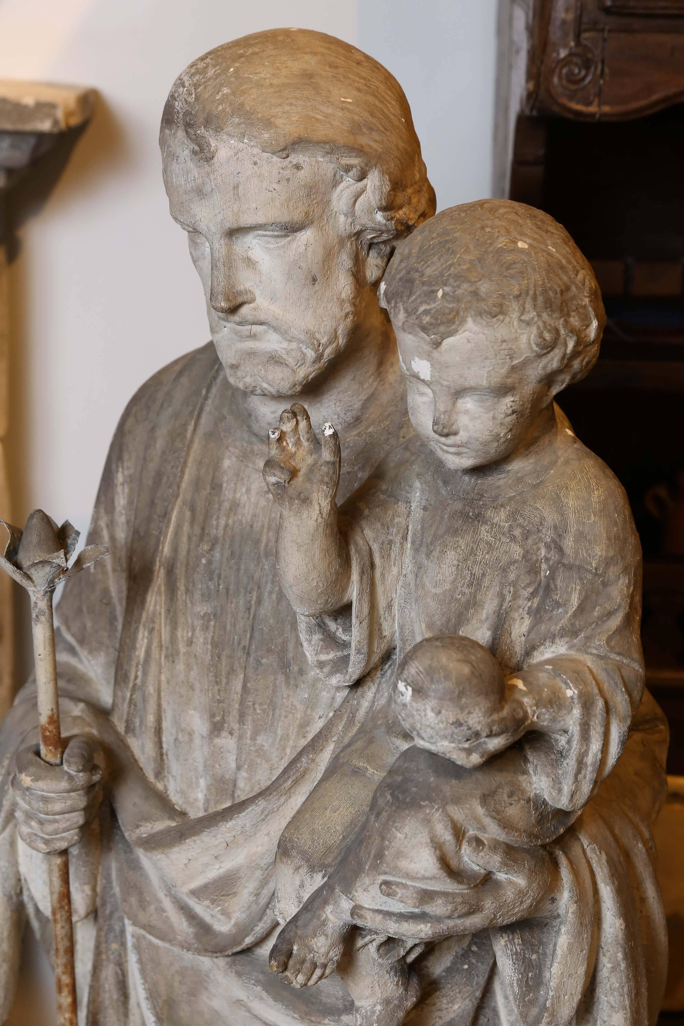 An impressive concrete statue from France of Saint Joseph holding the Baby Jesus. Saint Joseph, the Protector of the Catholic Church, holds an iron staff topped by a Lily in his right hand while holding the Christ Child with his left. The Baby Jesus