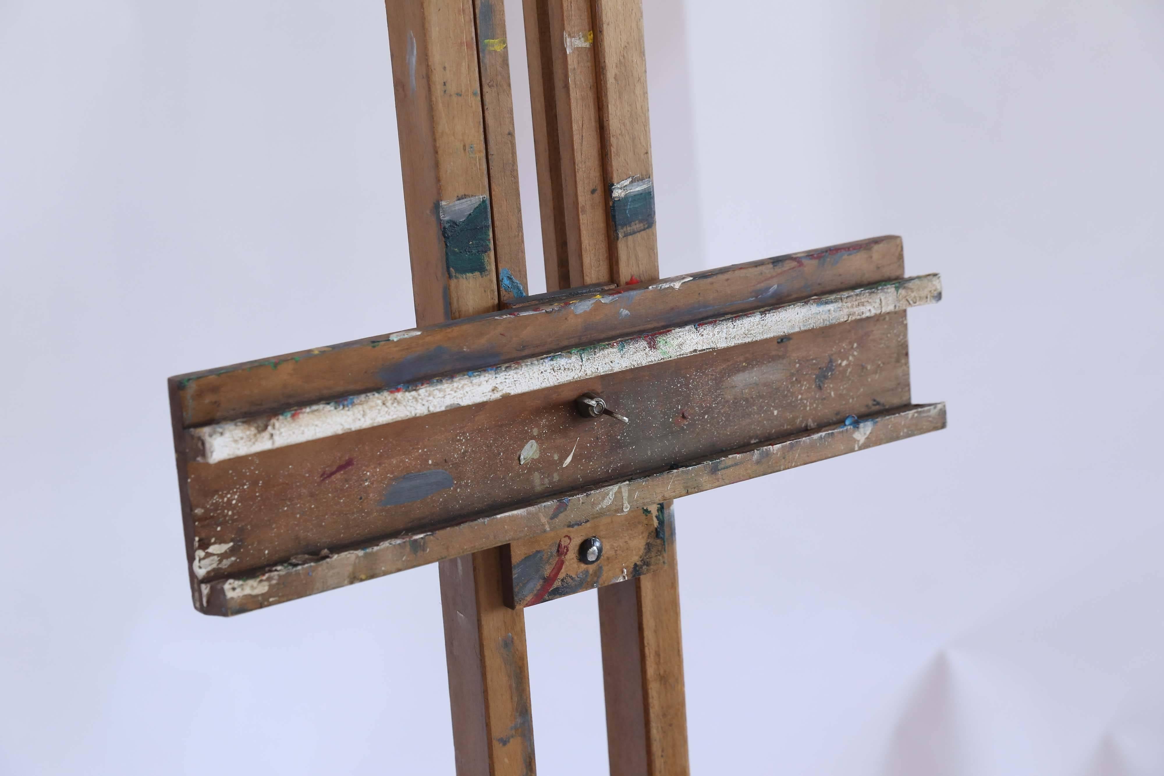 A vintage painter's easel from an art school in France. Made of wood, the easel has an adjustable tilt and the front clamps allow for supporting a canvas of almost any size. Splashes and drips of paint in a multitude of colors give a glimpse of the