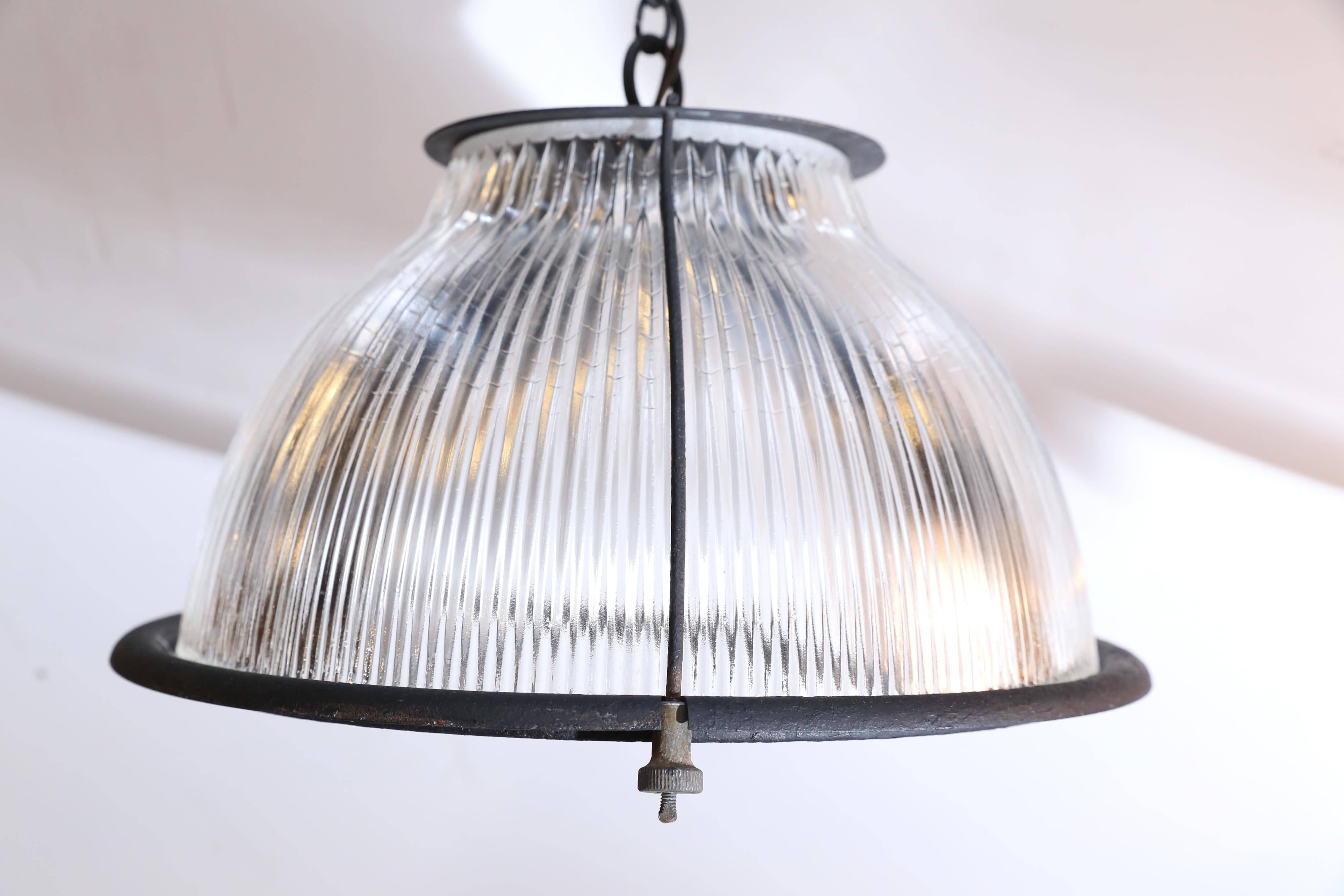 Industrial pendant light fixtures from France. With a timeless Industrial aesthetic, this vintage hanging light fixture has a metal frame supporting a ridged Holophane glass shade. The shade is suspended from a 55 inch pendant consisting of three