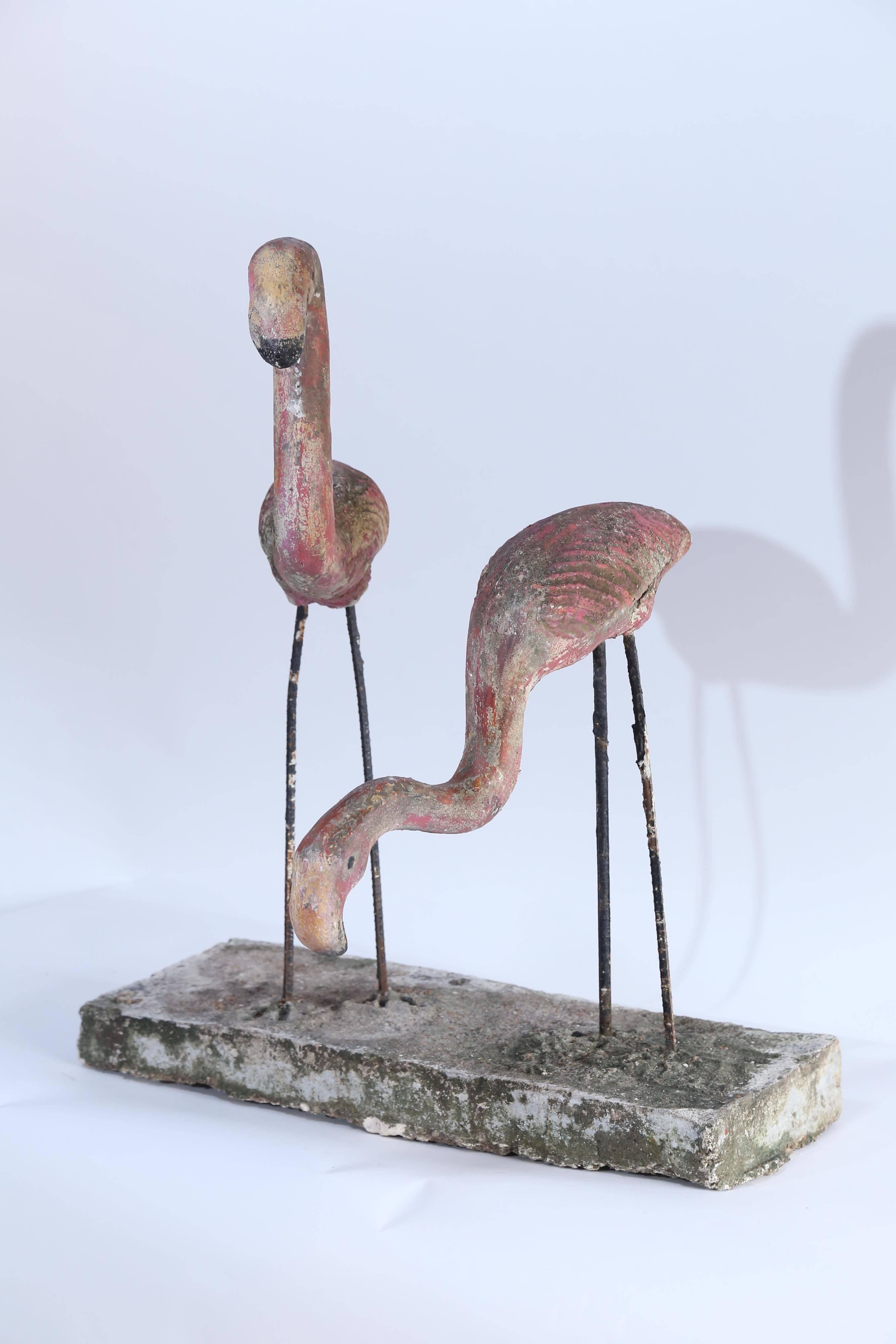 An iconic pair of flamingos to add fun to any garden. Made of concrete and standing on legs of re-bar encased in a concrete block, the birds retain traces of their original pink and fuchsia paint. The upright bird measures 20 x 6 and stands 29