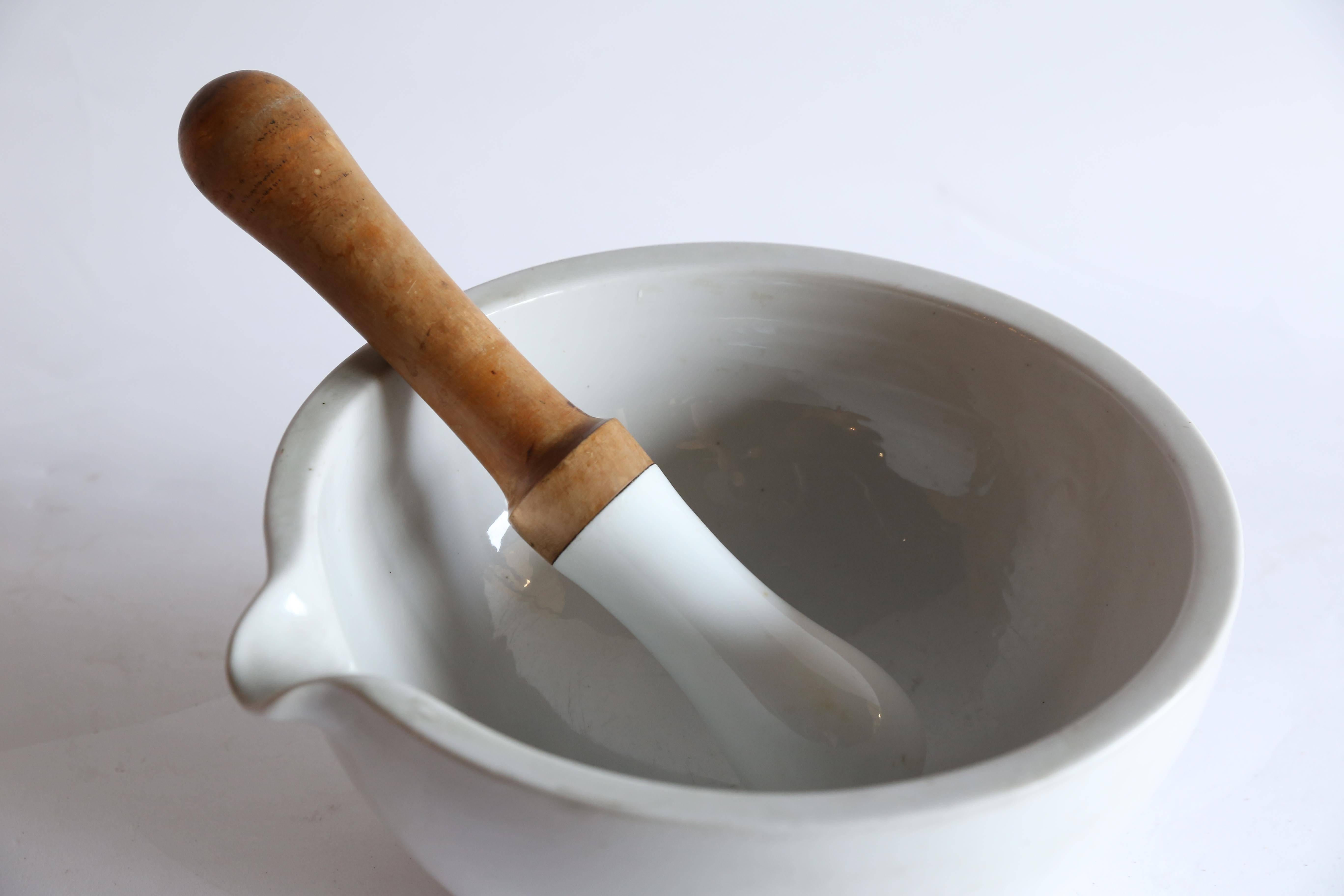 A generous porcelain mortar and pestle from France. The porcelain surface of the mortar is in nearly pristine condition with no chips or scratches. The wooden handle on the 12.5 inch porcelain pestle does have a small split that does not detract