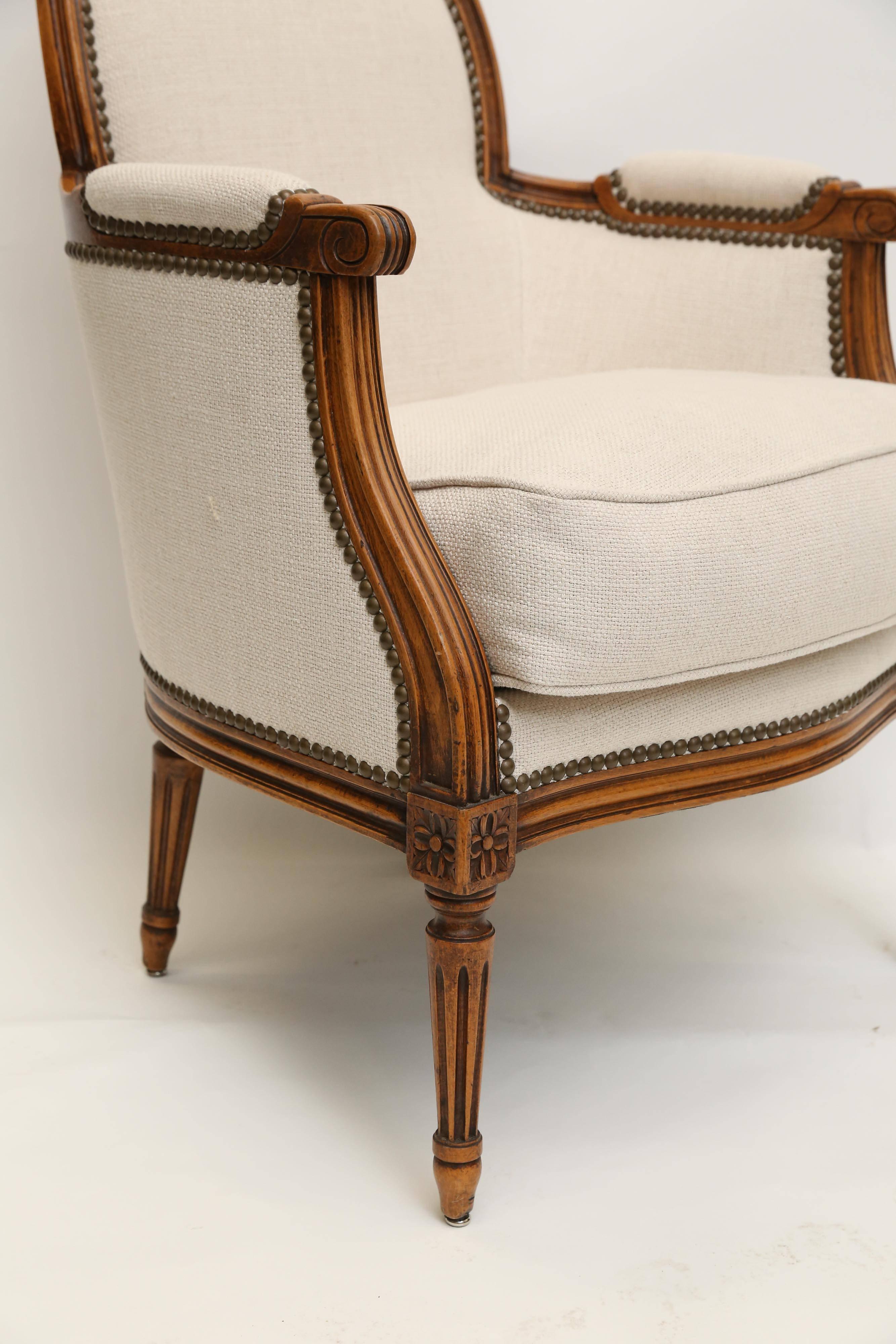 A striking Bergere chair from France. Newly upholstered in a white linen blend with brass nail heads, this small scale Bergere has beautiful proportions and a unique warmth. 
