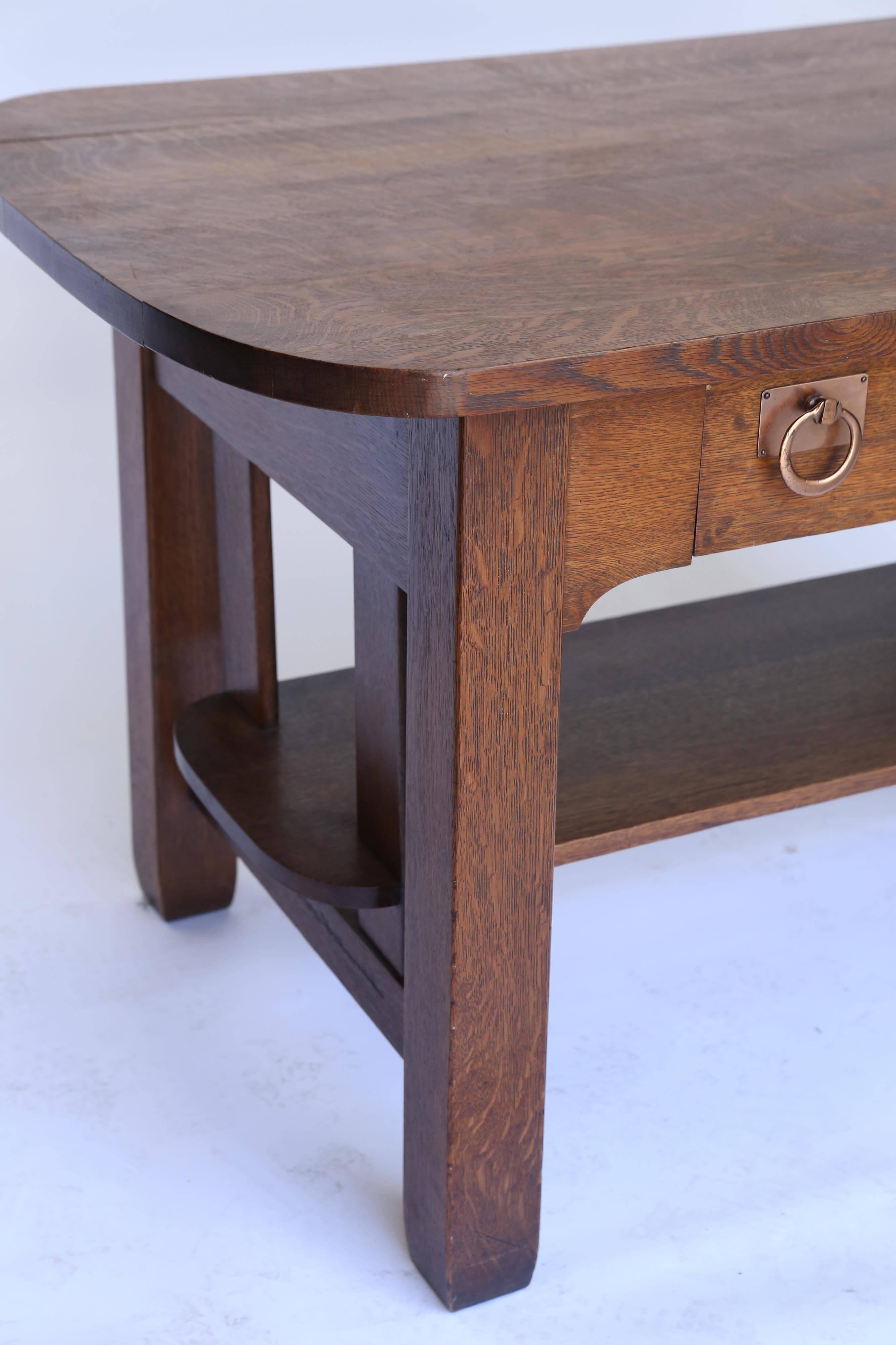 The iconic Craftsman look in an oak library table. Simplicity of form marked the era and this handsome table is exemplary of the movement. Strong bold legs support a lower shelf and the racetrack top; the single drawer sports the only ornamentation