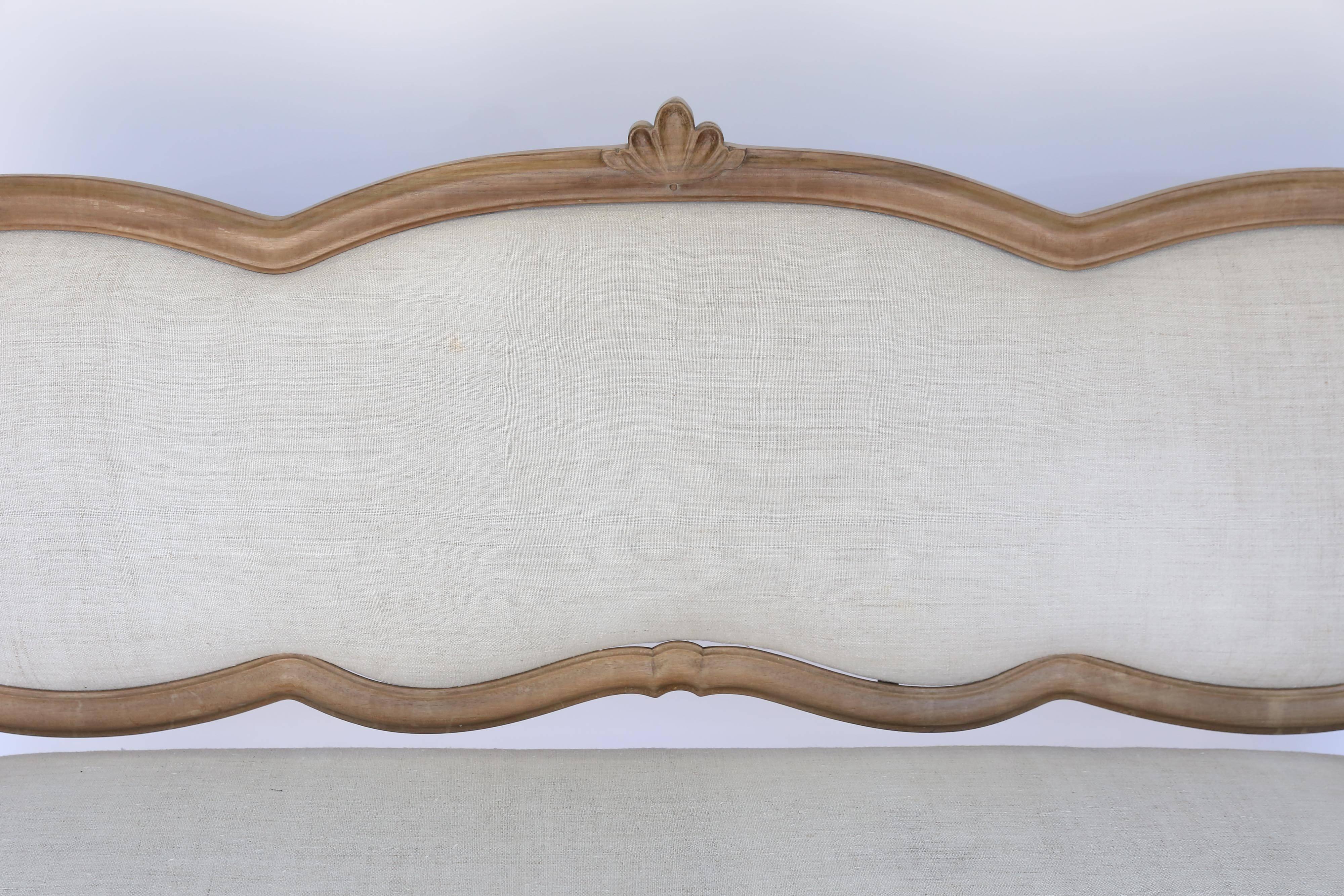 An exquisite bench or armless settee from France. Newly upholstered in linen, the graceful, flowing lines and the beauty of natural wood make this an eye-catching and captivating piece.