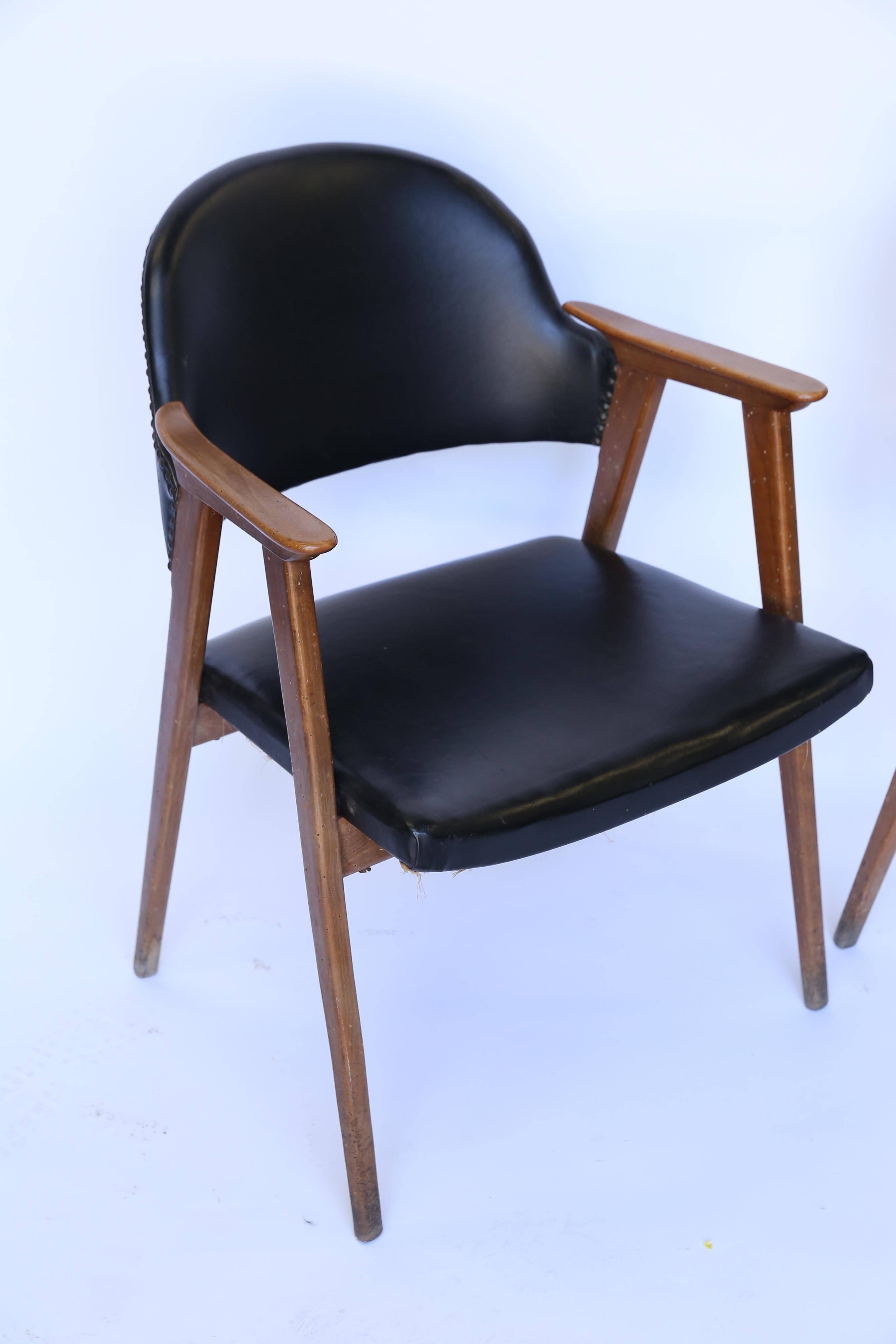 A handsome pair of midcentury armchairs from France. In black leather with brass nail head detailing on the back and a sculptural form. While the leather is in near perfect condition, the wood has experienced a minor worm infestation which is no