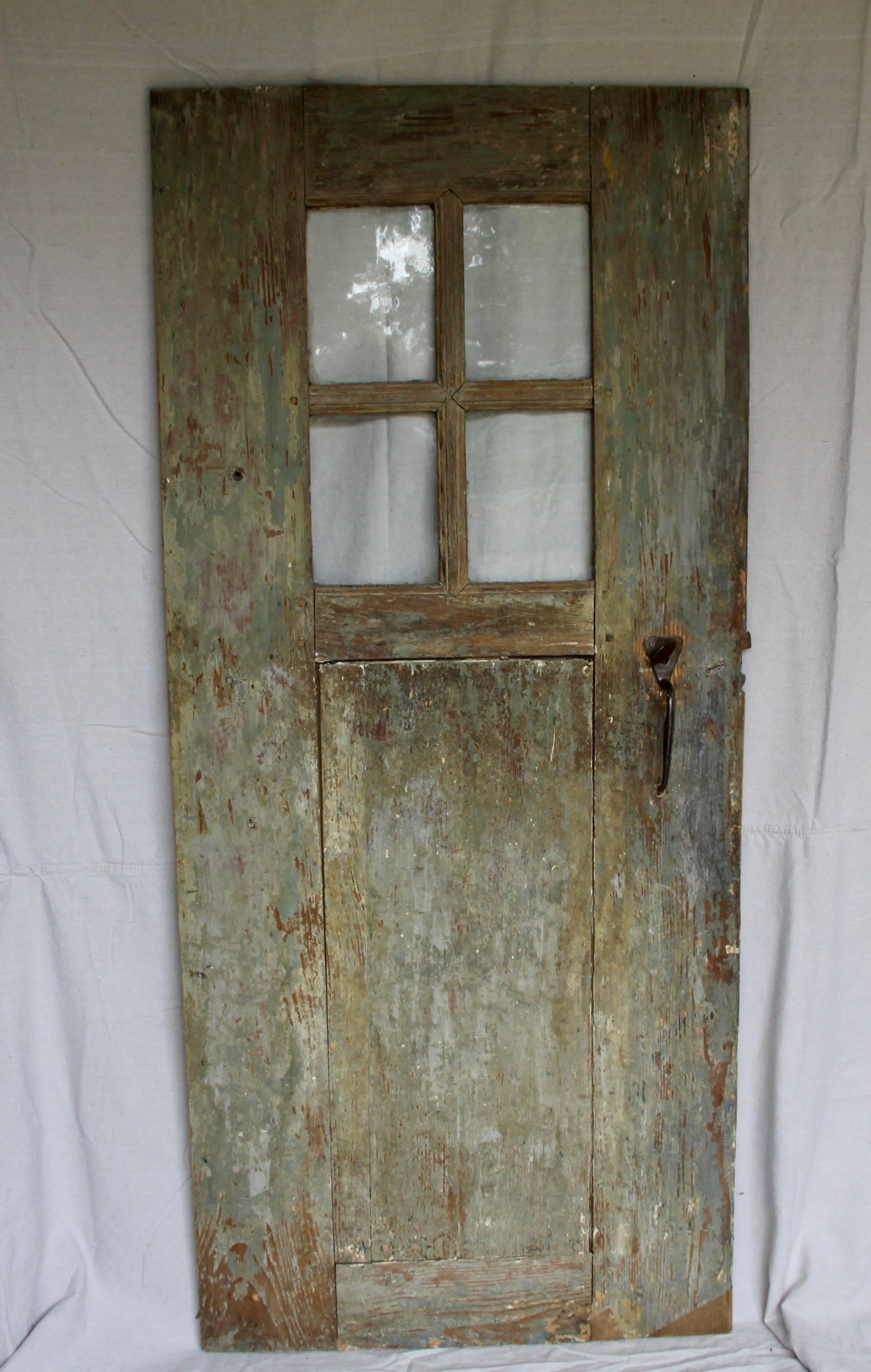 Utterly charming and curious, a very old door of unusual size. Handcrafted and retaining traces of the original green paint and iron thumb latch hardware, it's unusual size and beautiful wavy glass give this door a magical quality.