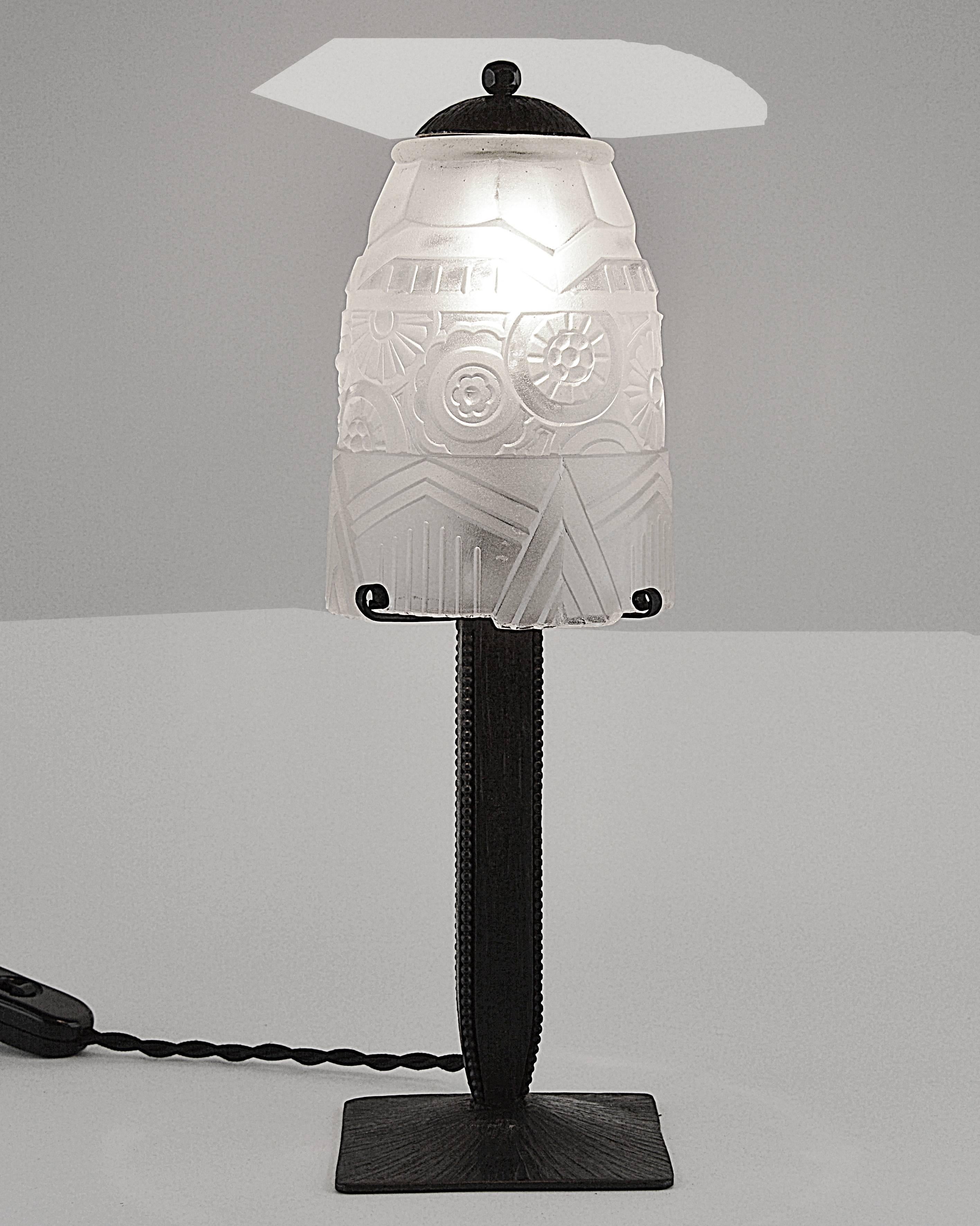 French Art Deco table lamp by the ironworker Charles Piguet, Lyon, France, circa 1925. The precious base comes with its frosted molded-pressed glass shade, very well defined. This shade is very close to the Muller Freres, Daum and Edgar Brandt's