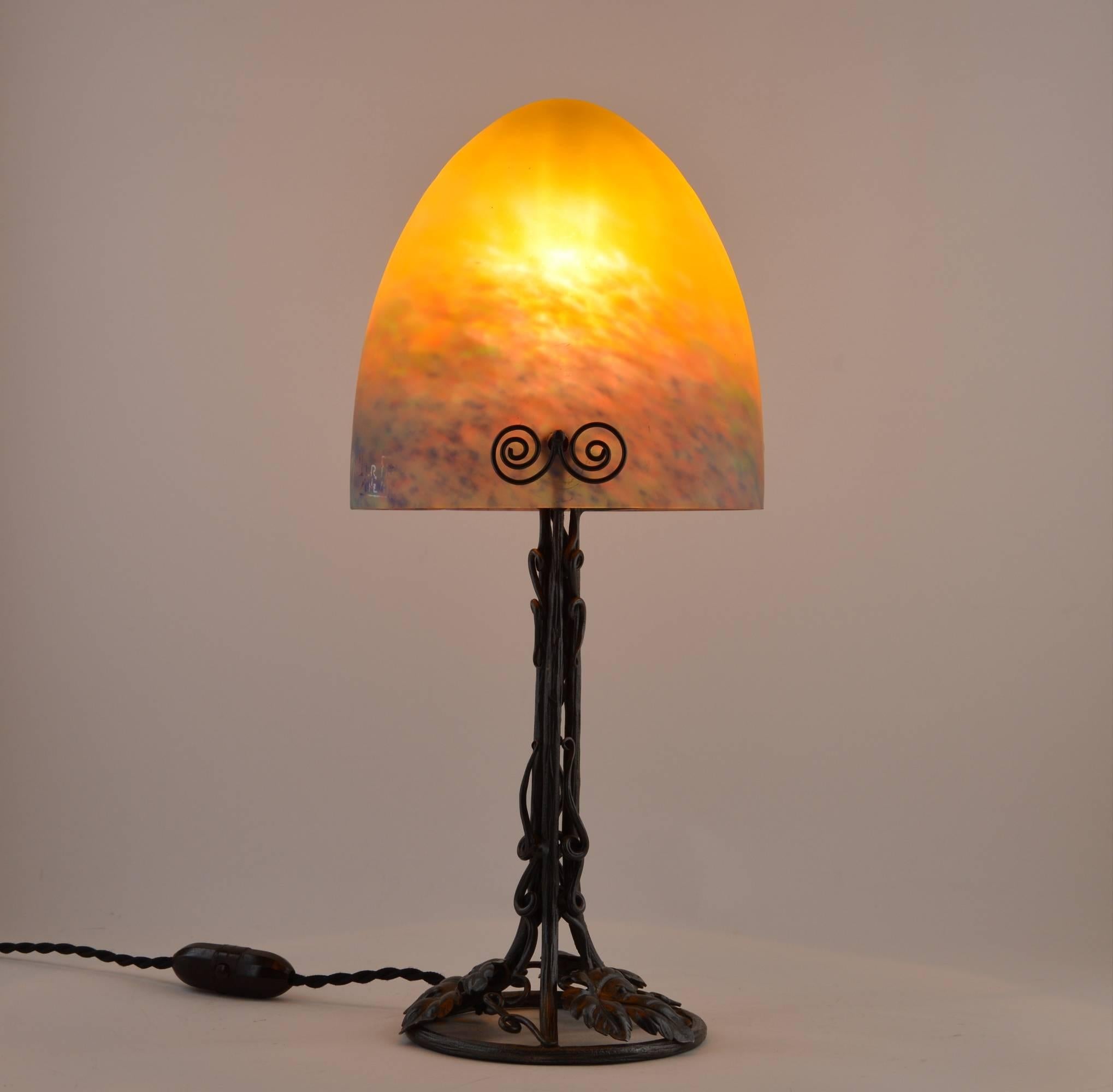 French Art Deco table lamp by Muller Freres, Luneville, early 1920s. The shade is made of blown double glass with powder applications between both layers. Colors are dark yellow, blue, turquoise blue and pink. On an exquisite wrought-irin base.