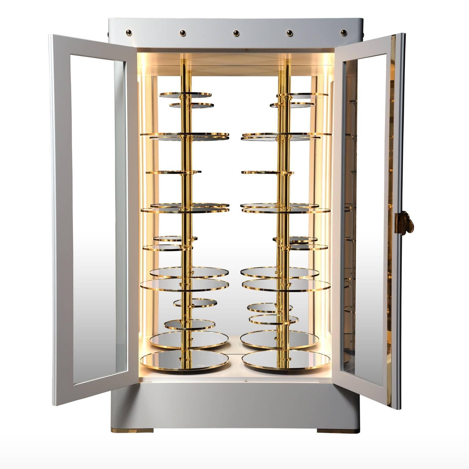 Collector‘s cabinet , satin white lacquered structure and polished brass. Gold-plated handle with swivel wing to access to the locker. Interior consists of two columns and 14 circular swivel shelves and brass mirror. LED Lighting included.

The