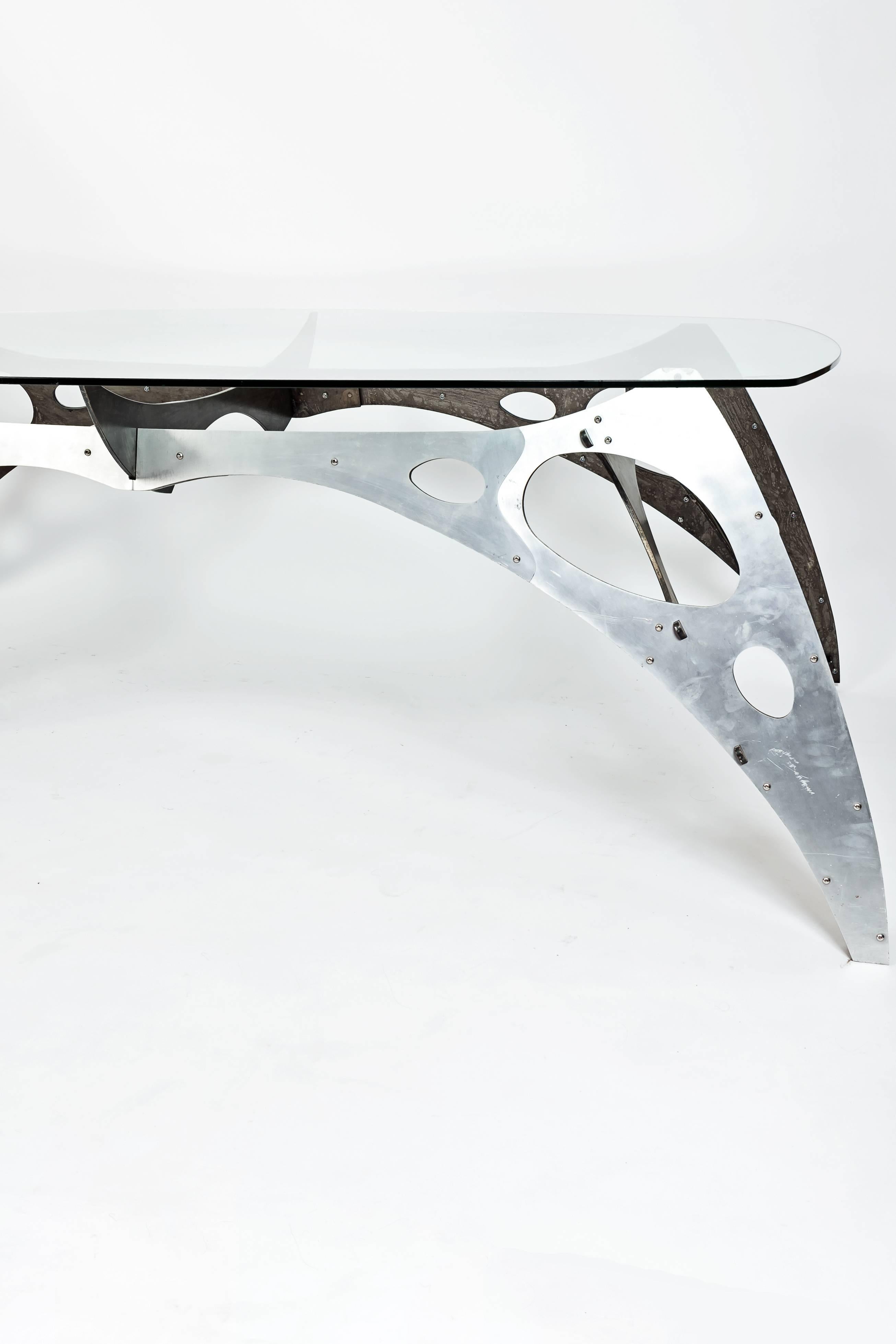 Aluminium dining table with aerodynamic design. The top glass has an oval form.