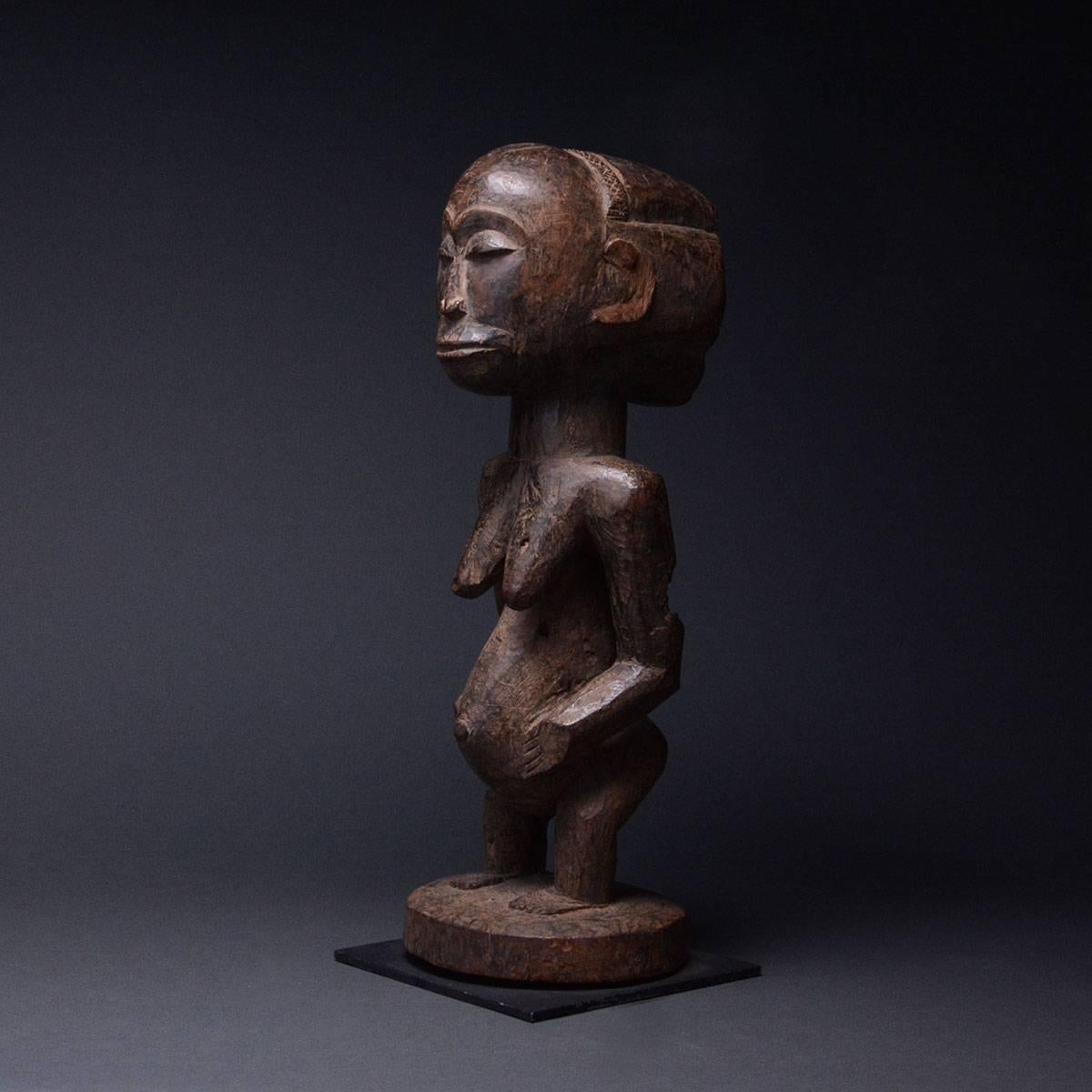 This powerful and well-used sculpture of a standing female is an ancestor figure from the Hemba group of what was once Zaire. Female figures are markedly less common than male versions, as most figures represent the male founders of tribal clans