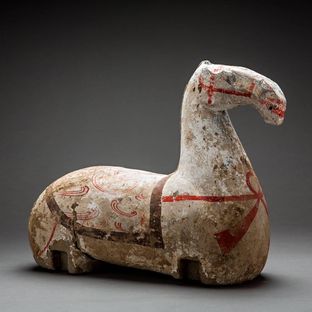 This powerfully modeled torso of a horse is painted with a full harness in red and white pigment. The saddle is outlined in blue paint and decorated with red circular designs. Staring eyes, bared teeth and flared nostrils, the horse’s expression is