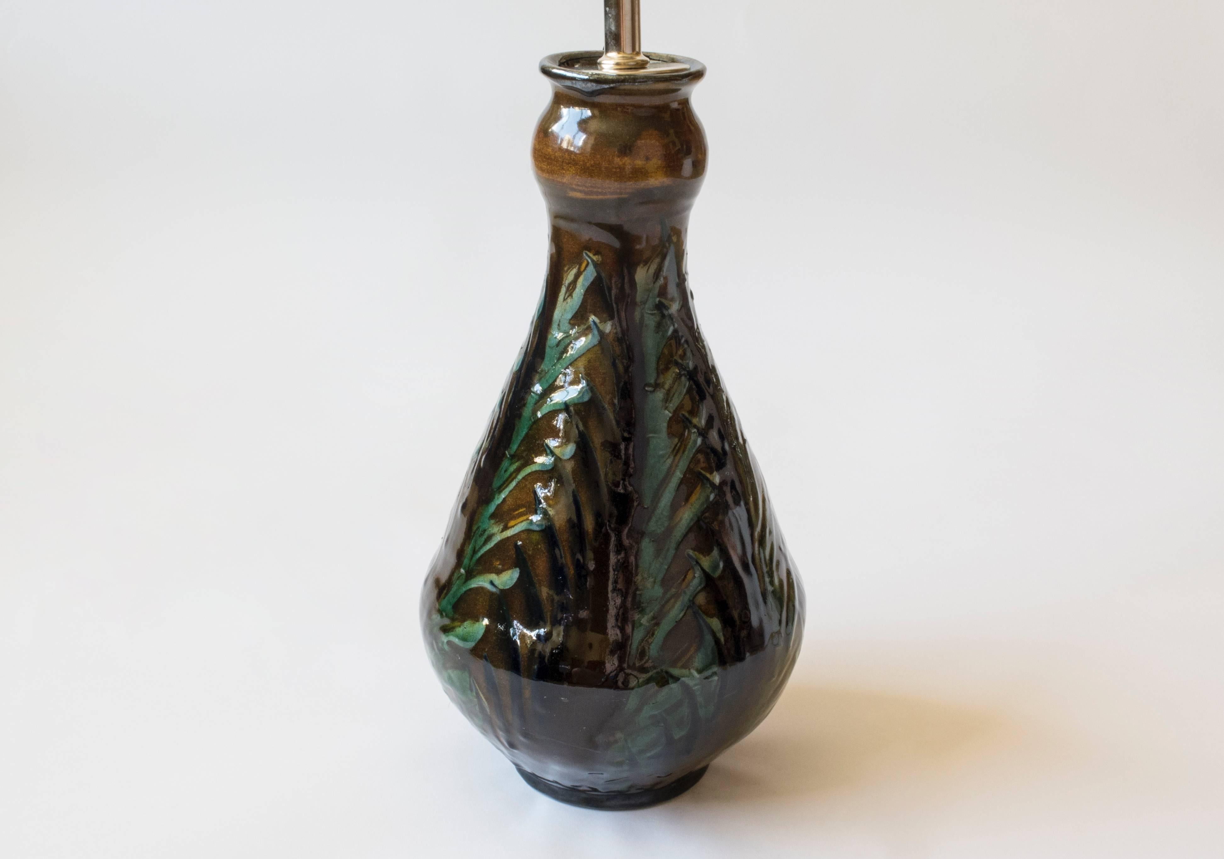 The radiant glaze composed of foliate patterns painted in variegated greens and browns against a caramel-colored background. The garlic-mouth form, on a circular foot, signed underneath: HAK. 

An unusual and handmade Chinese inspired form from