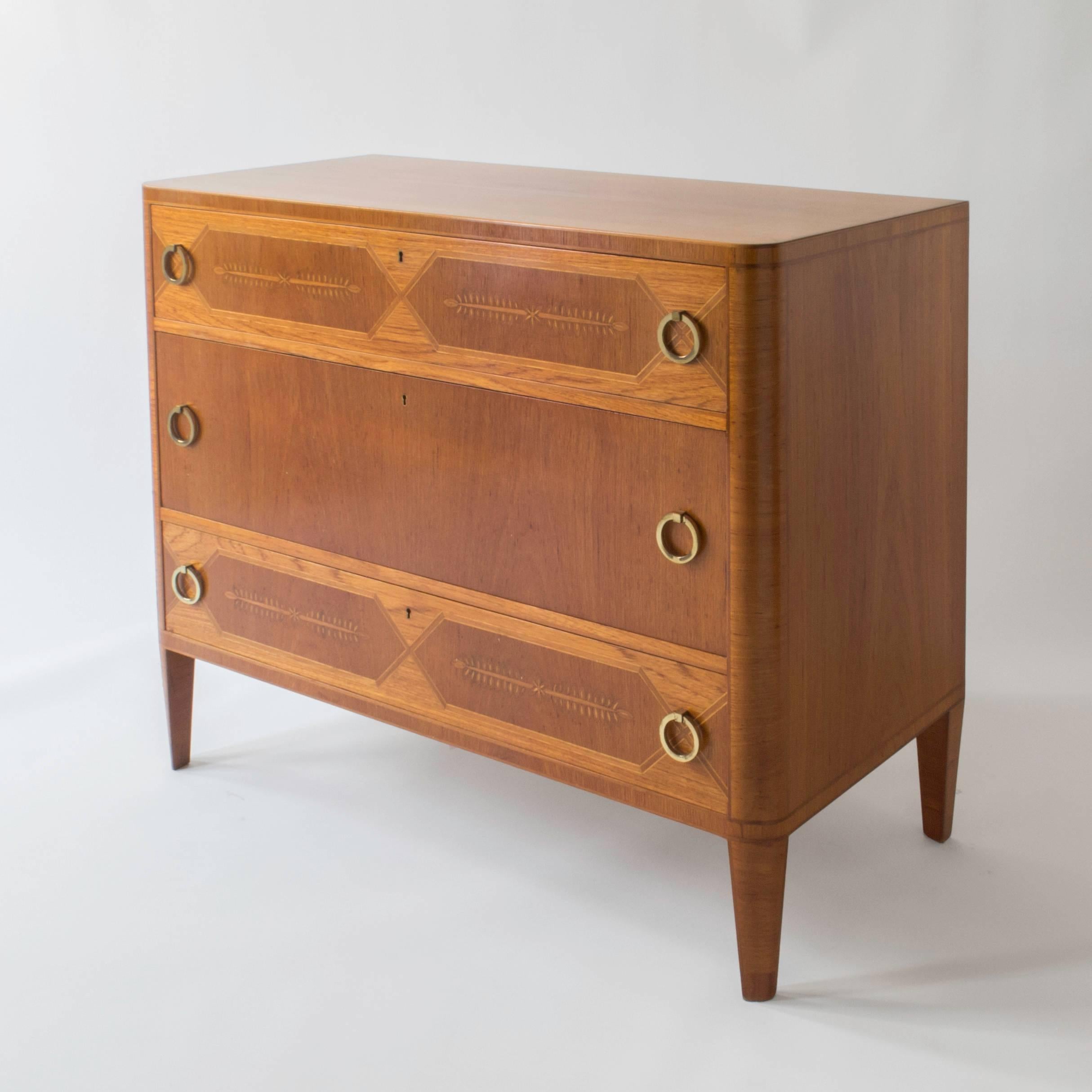 A subtle, beautifully constructed and highly sophisticated piece.

The rectangular top with rounded front corners, above three stacked drawers, the top and bottom drawers displaying x-form reserves centring stylized garland marquetry, the exterior