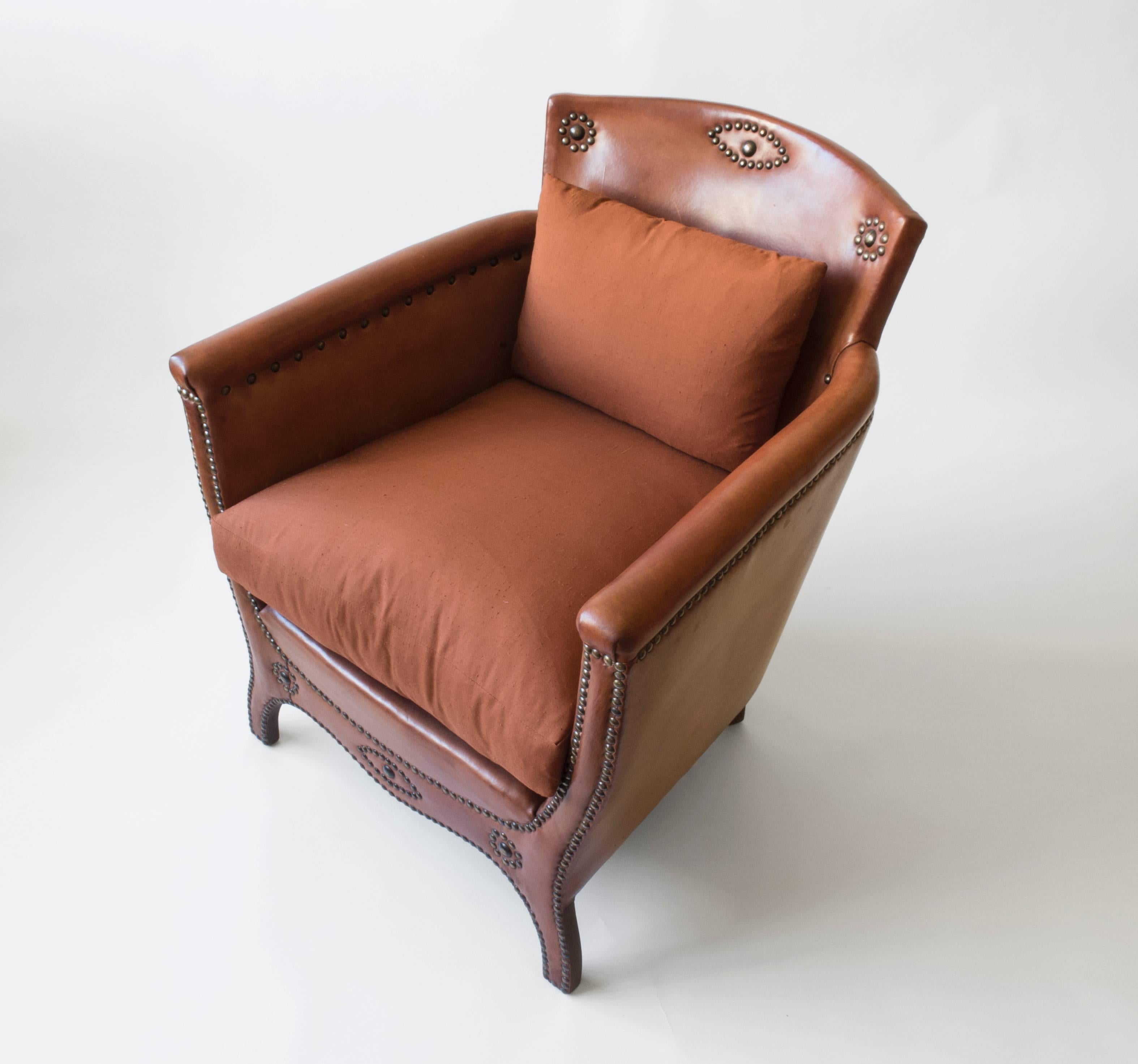 Retaining beautifully preserved and patinated leather, adorned in original decorative brass nails, and newly upholstered in raw silk over comfortable down-stuffed cushions. This compact armchair is a rich and stylish addition to any room. The arched
