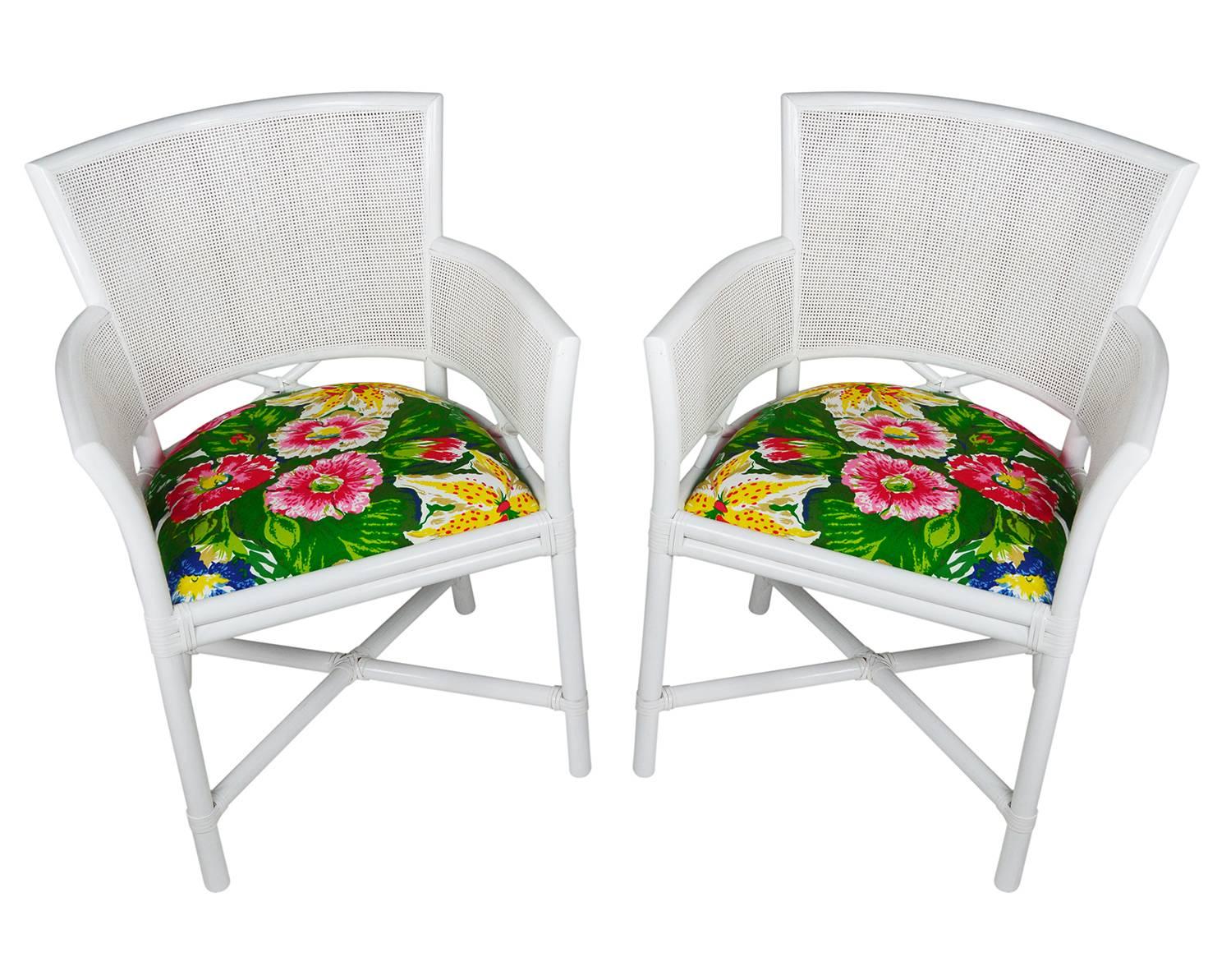 Pair of Ficks Reed armchairs newly lacquered in white. The sleek rattan frame has a caned back and leather windings. The new seat cushion is upholstered in Dorothy's Garden by Dorothy Draper Co.