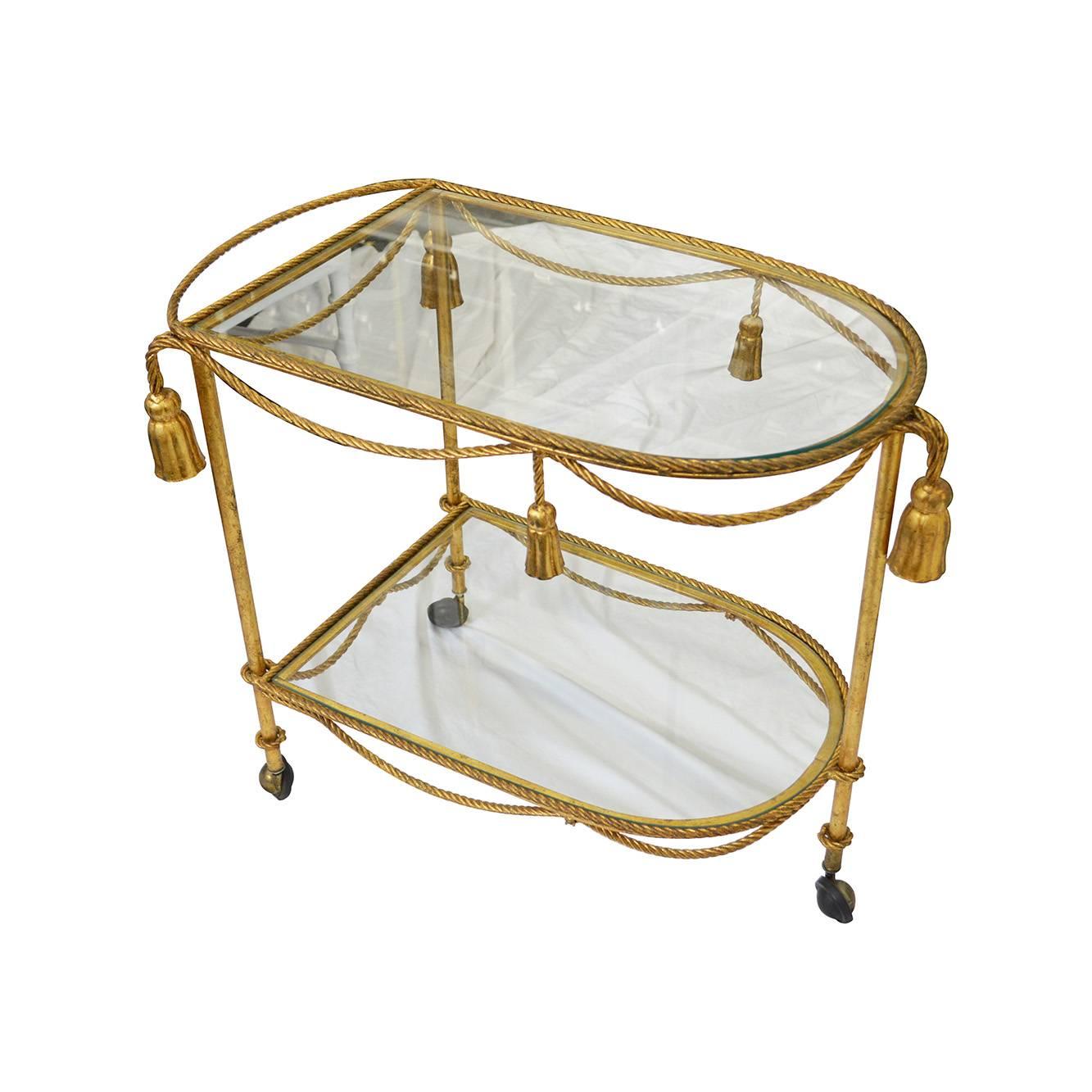 Vintage brass Hollywood Regency tea cart mounted on three caster wheels with rope and tassel detailing and glass inlays.