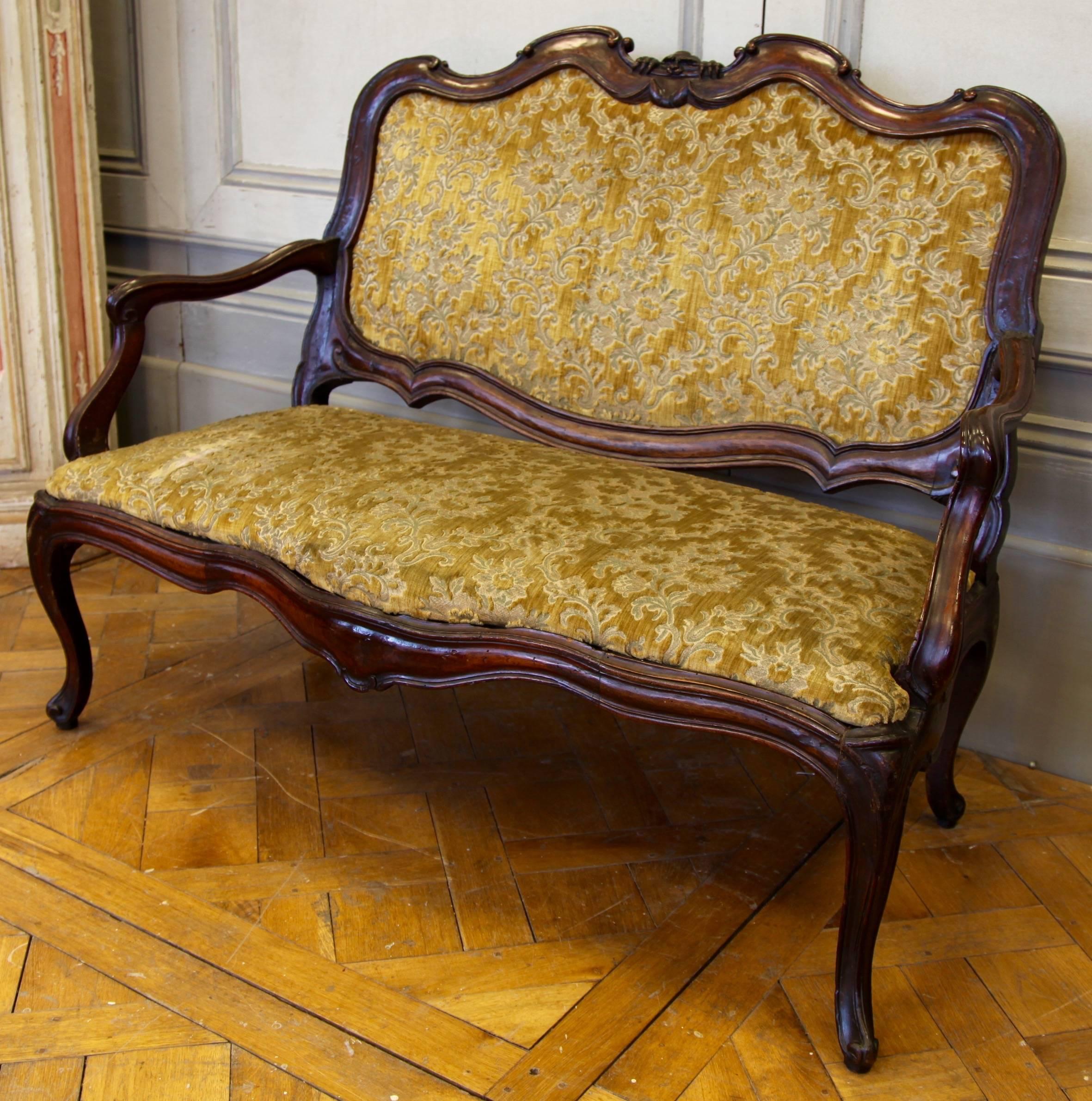 Beautiful 18th century Italian sofa in carved walnut. Has the detail of an impish sprite in the carving at the centre of the backrest which, typical of its period, would have been a talisman for protection. Upholstered in a golden velvet damask.