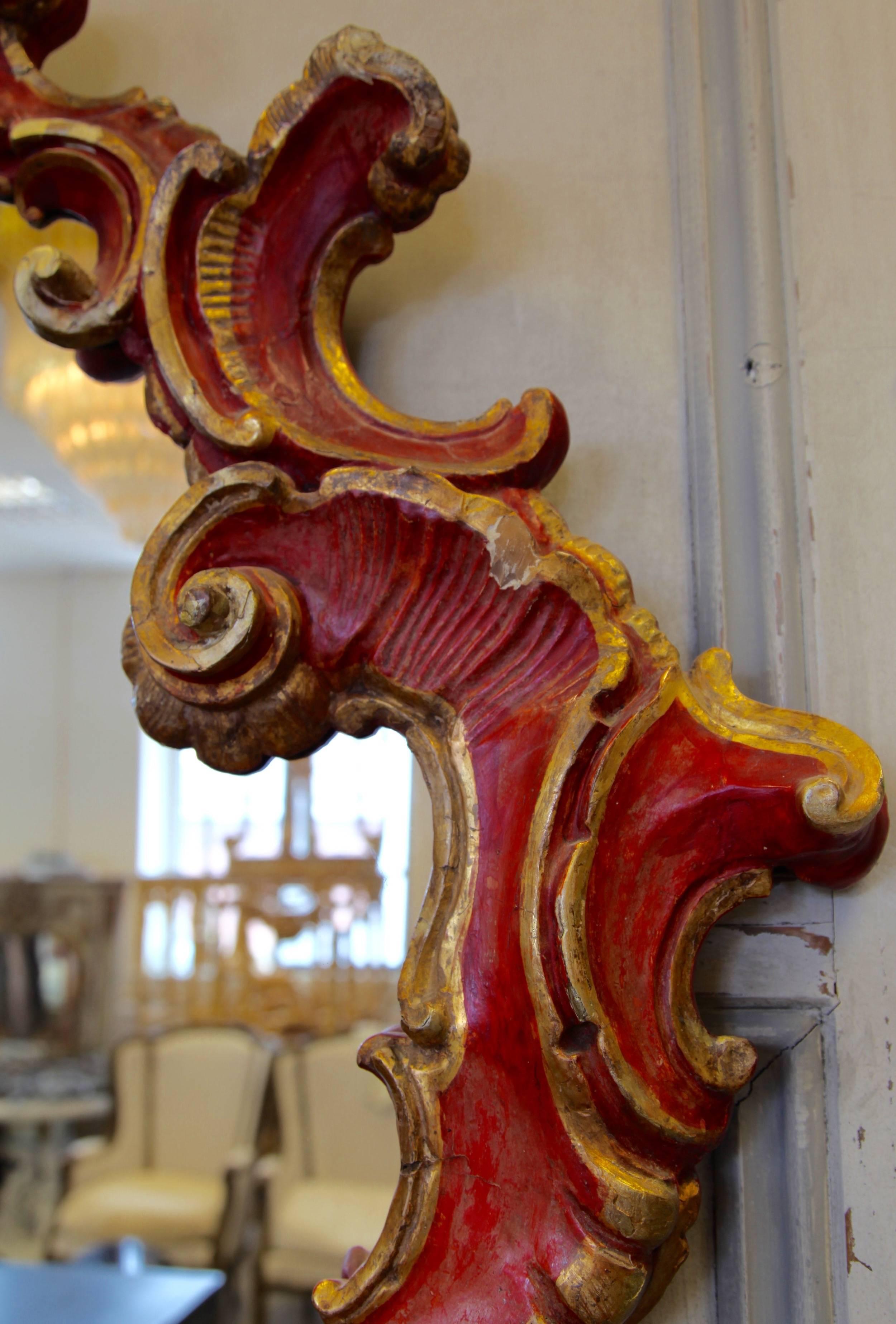 An 18th century Venetian mirror hand-carved in wood with original patina, finished in a deep red and gilded high lights. A beautiful and rare find.