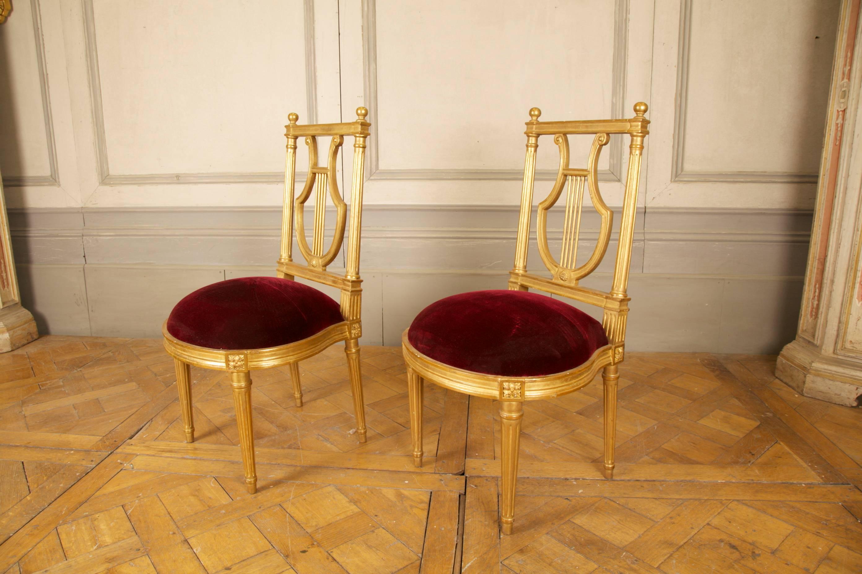 A pair of Louis XVI style chairs. Hand-carved in beech wood with a classical lyre motif forming the the back rest and finished with a hand gilded, lightly aged and distressed, patina.