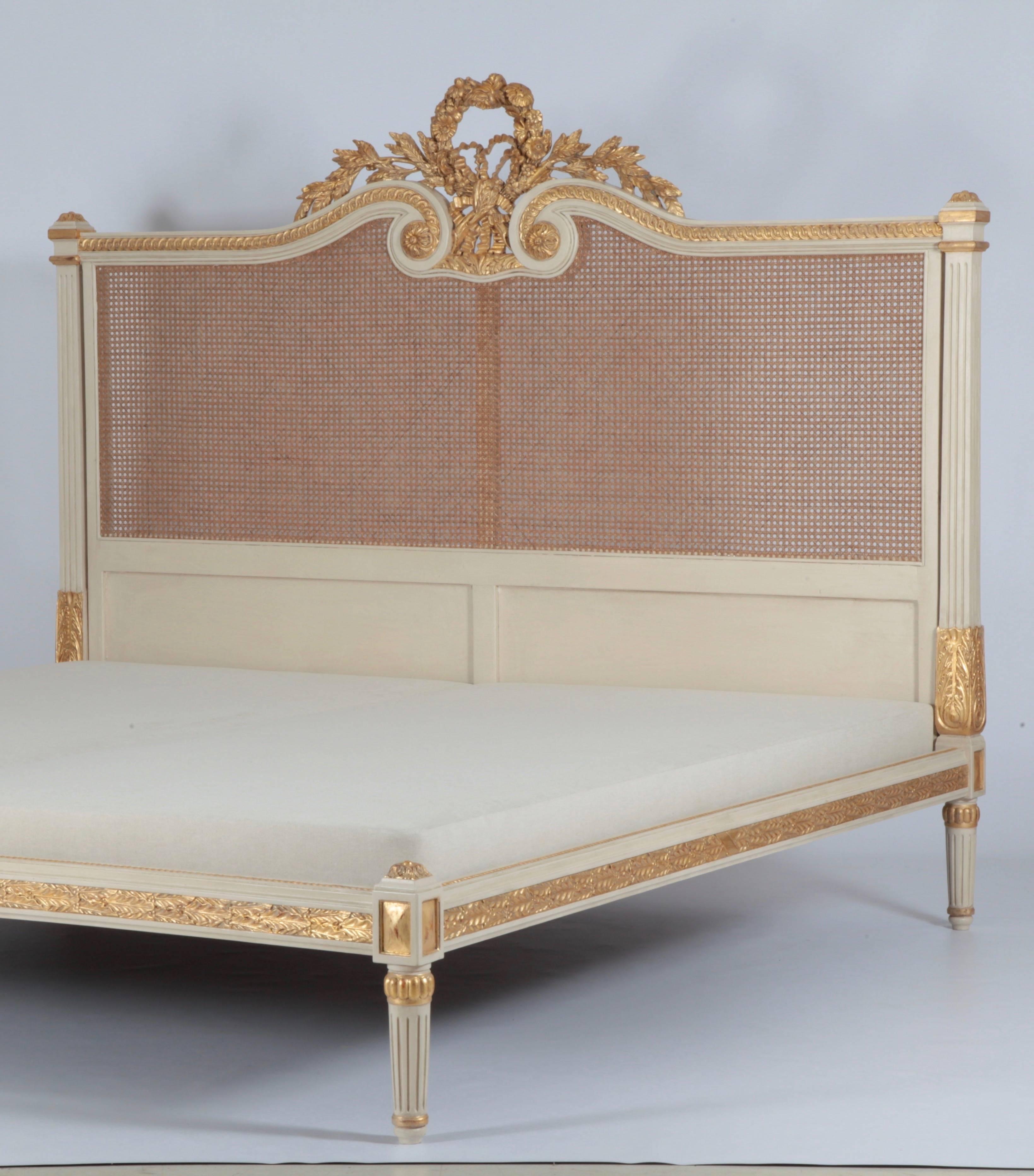 Louis XVI style bed intricately carved by hand depicting a central motif of garlanded flowers with ribbons and bayleaves on the headboard continued around the frame of the bed. Finished in two tones of Provençal white and hand gilded highlights with