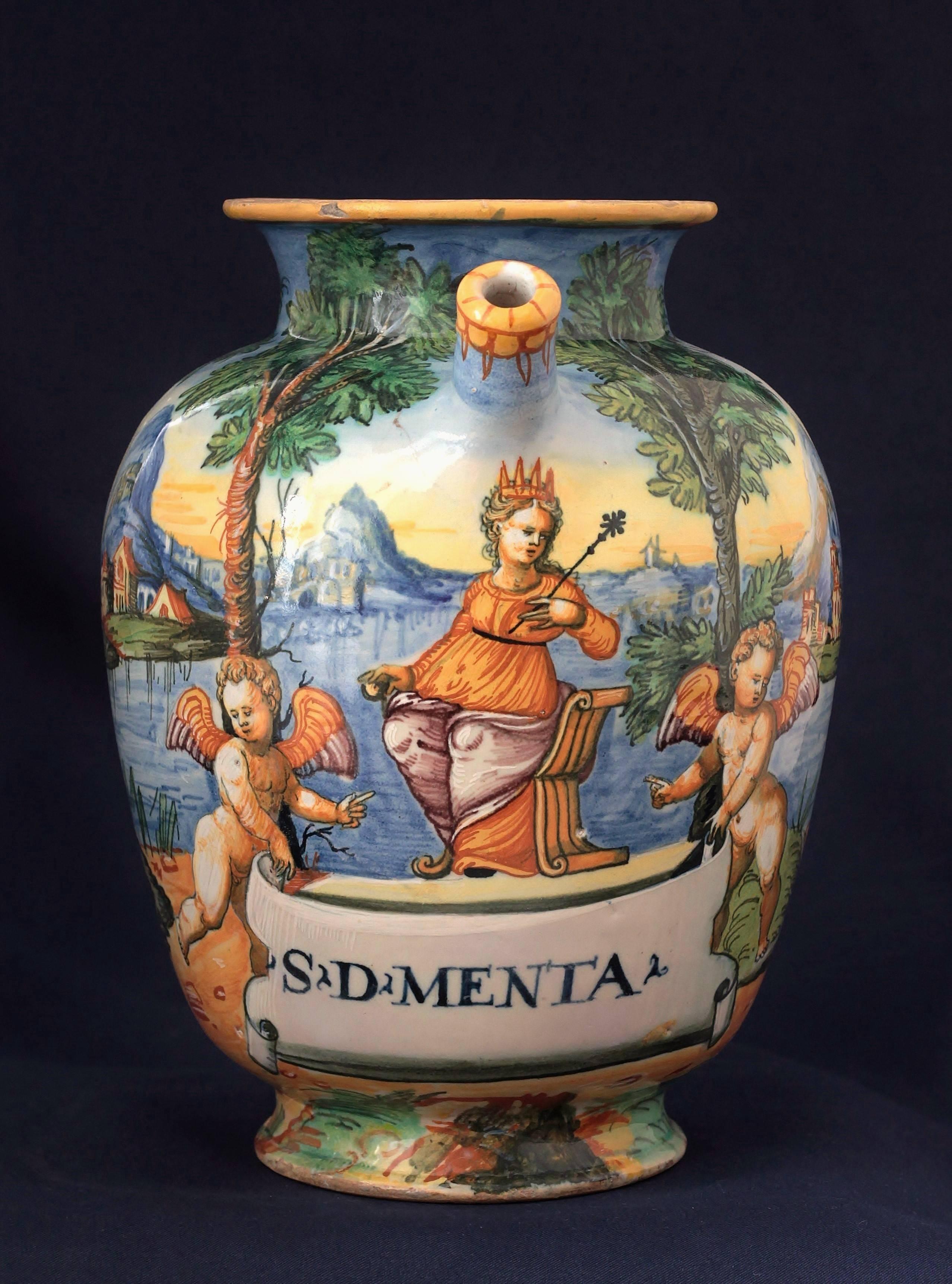 An Urbino Majolica chevrette with polychrome decoration “a istoriato” representing a queen with two cupid in a landscape. Apothecary inscription : “S.D.MENTA”.
Workshop of Orazio Fontana, circa 1565-1570, 16th century.
Measures: H 22.5 cm, D 20