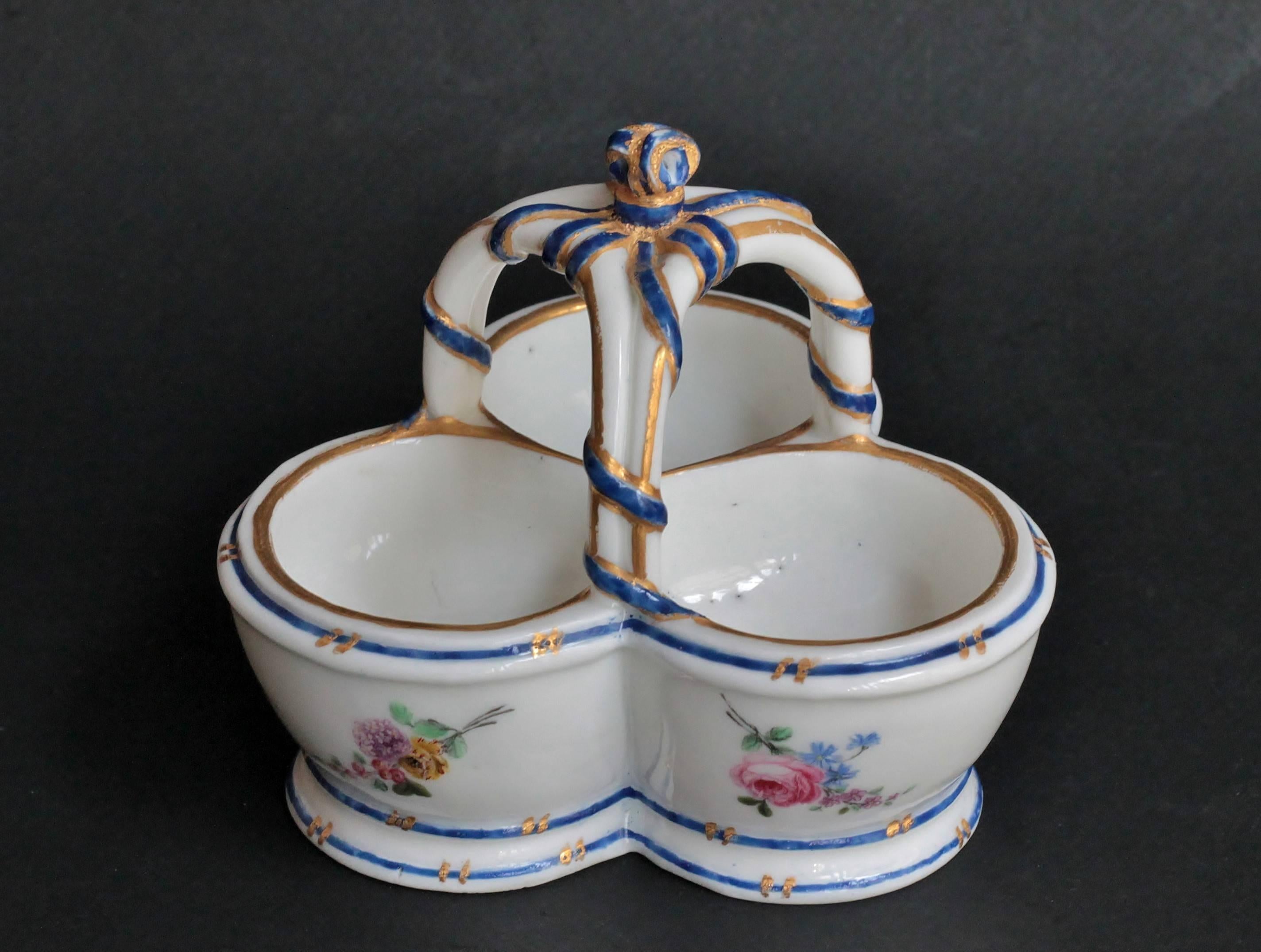 A Sèvres triple salt in porcelain painted with flower sprays and blue line borders with gilt dashes, the handle interlaced with a blue ribbon and edged with gilding. Small traces of LL monogram in purple.
Measures: Height 8.7 cm, width 10.5 cm,