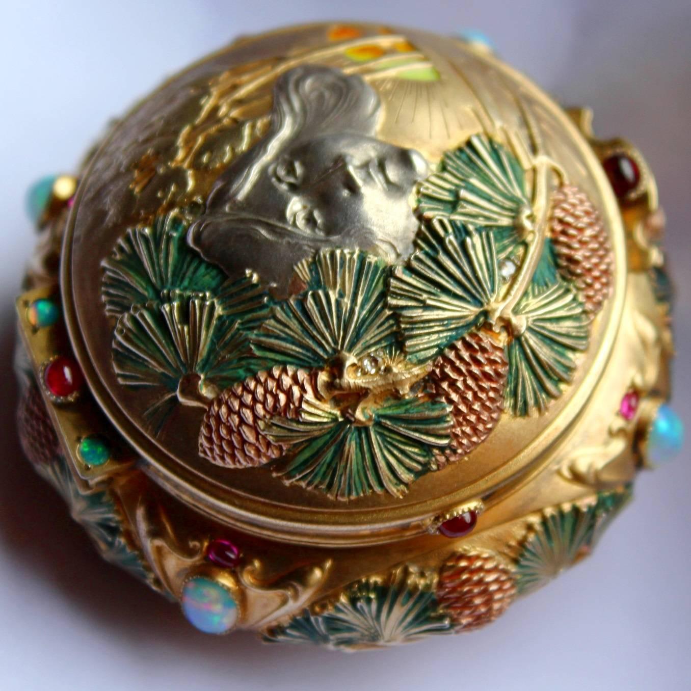 Rare and beautiful Art Nouveau silver gilt and enameled box, the cover decorated with a stylized head amidst pine cones with forest scene with enamelled rising sign, diamond chip to cover, the edge set with cabochon rubies and opals. In a fitted box