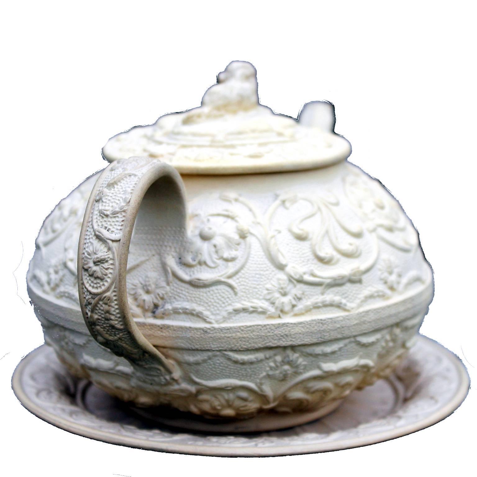 Rare Wedgwood biscuit ware teapot, cover and stand, circa 1840, the cover with a finial modelled as a recumbent King Charles Spaniel on a tasselled cushion, the body and handles finely decorated with scrolling leaves and flower heads, the stand with