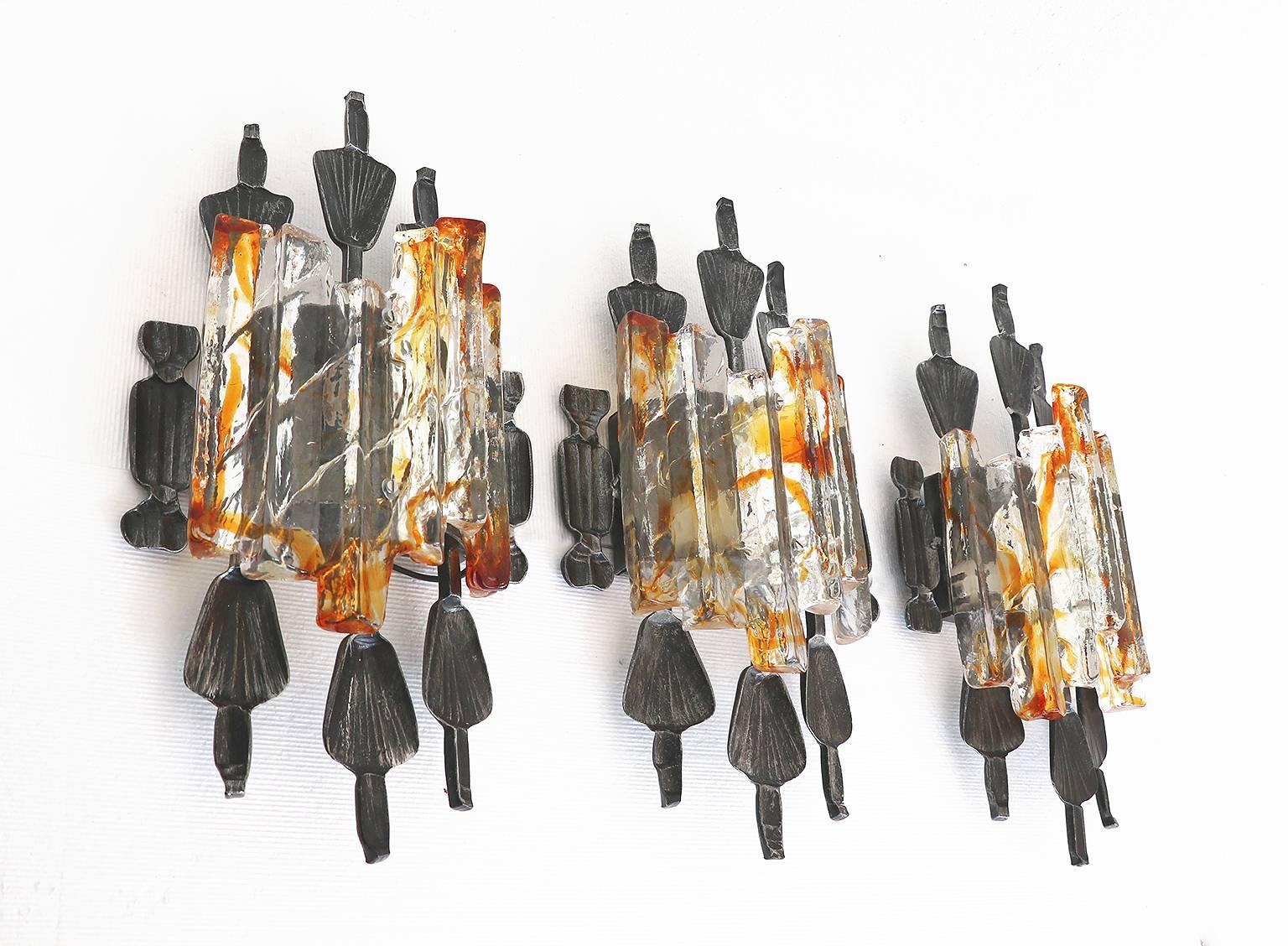 Elegant set of three brutalist wall sconces with clear and amber Murano glass on a metal frame. Designed by Tom Ahlström & Hans Ehrlich for A & E Design, Sweden in the 1960s.

Design: Tom Ahlstroem & Hans Ehrlich. 
Lighting: takes one large Edison
