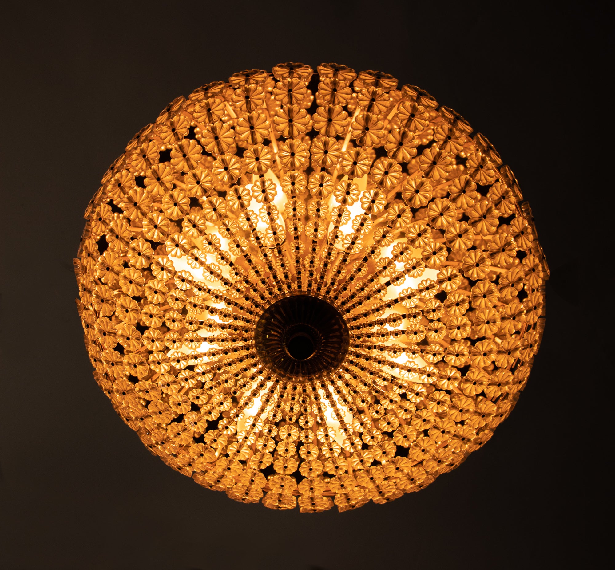 Gorgeous large starburst flush mount chandelier in mid-century style with countless crystal flowers on a golden brass frame. The glass flowers are reminiscent of a sunburst pattern. Rare design. The chandelier illuminates beautifully and offers a