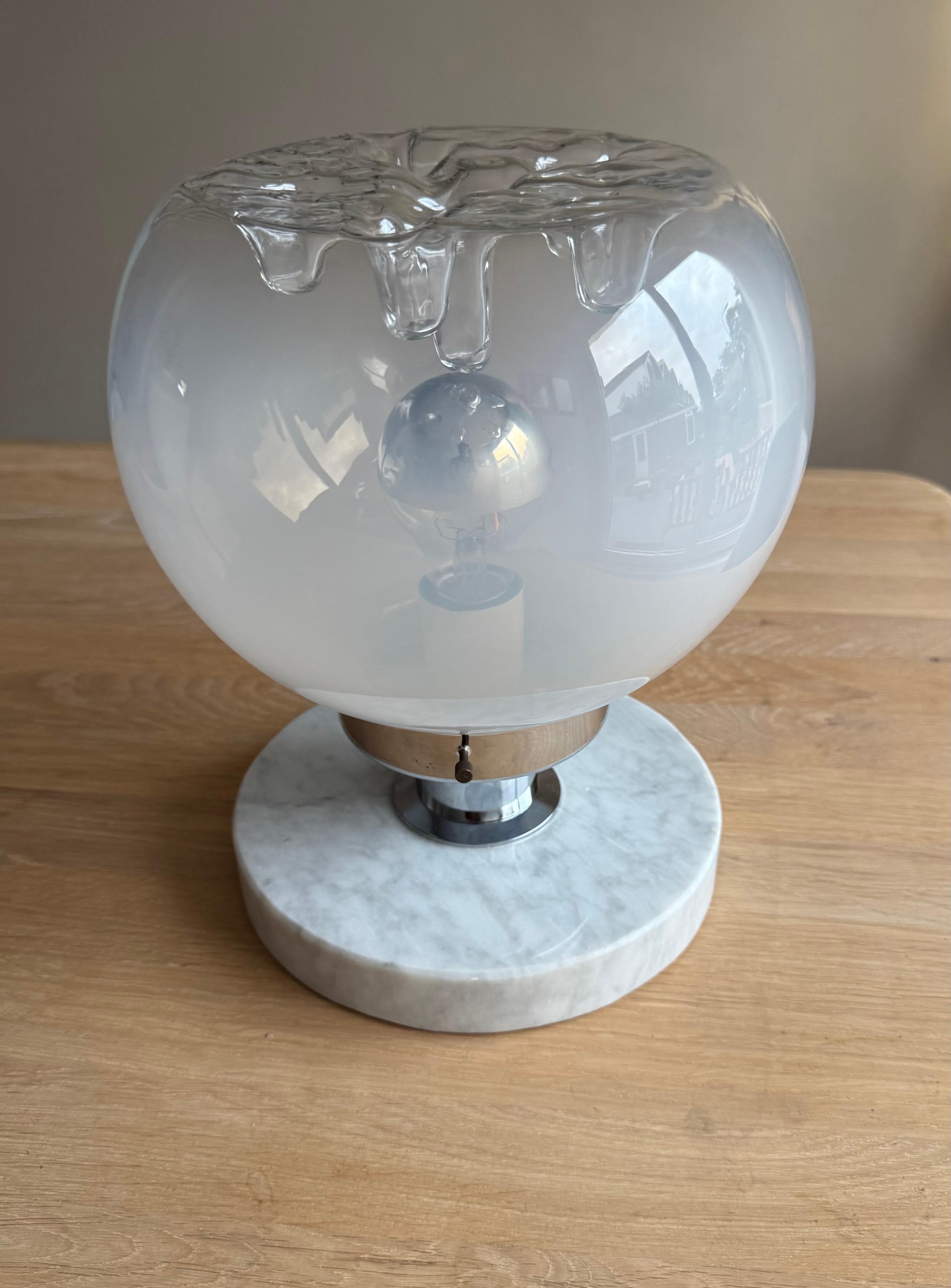 Llamativa lámpara de sobremesa de cristal de Murano de los años 70, fabricada a mano en Italia. Esta pieza escultórica presenta un globo de cristal soplado a mano con un cautivador acabado degradado transparente y esmerilado, coronado por una