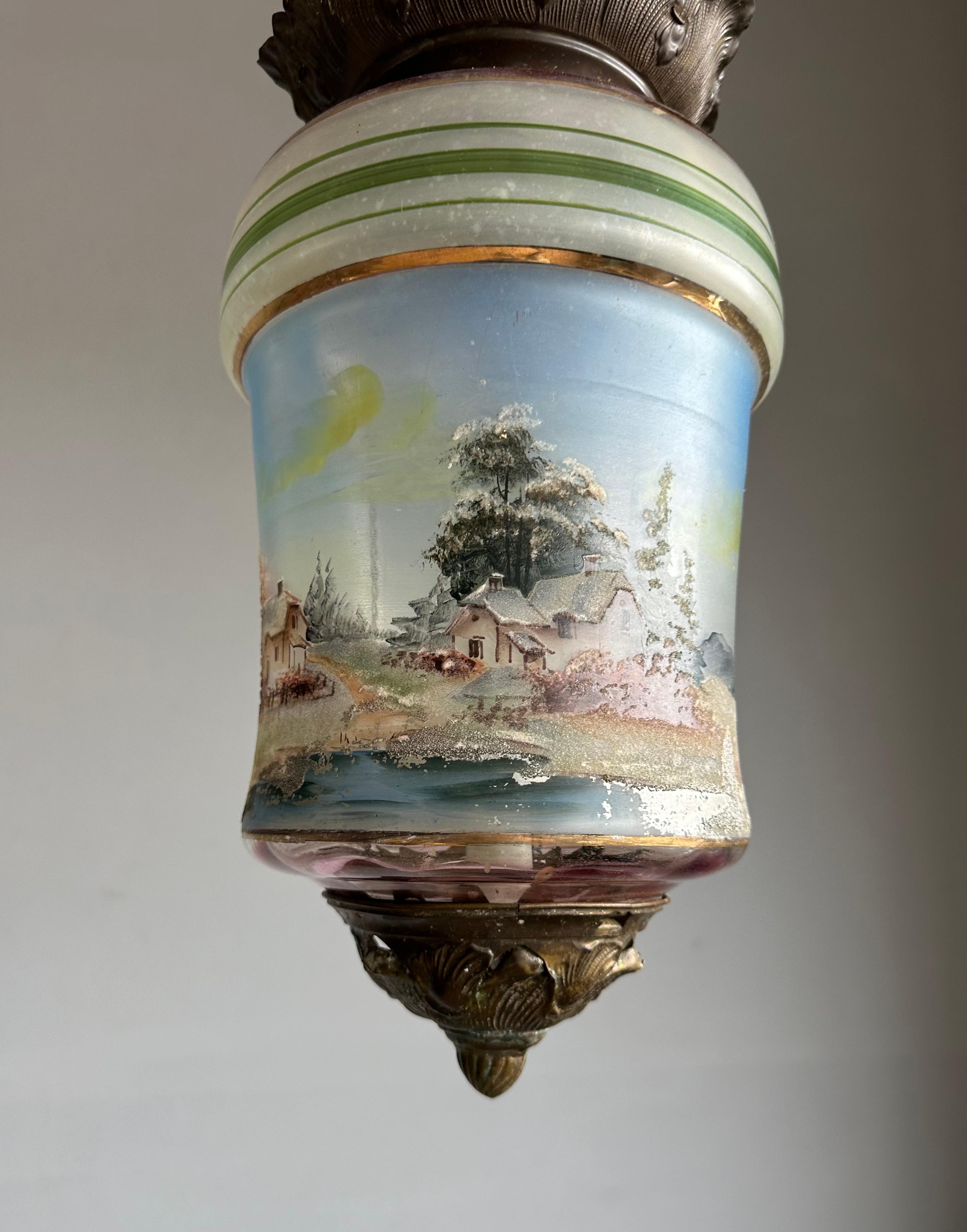 A rare and atmospheric pendant from the Victorian period (late 19th century), this hanging lantern showcases exquisite craftsmanship and timeless charm. The hand-blown glass shade is decorated with a continuous 360° pastoral lake house scene,