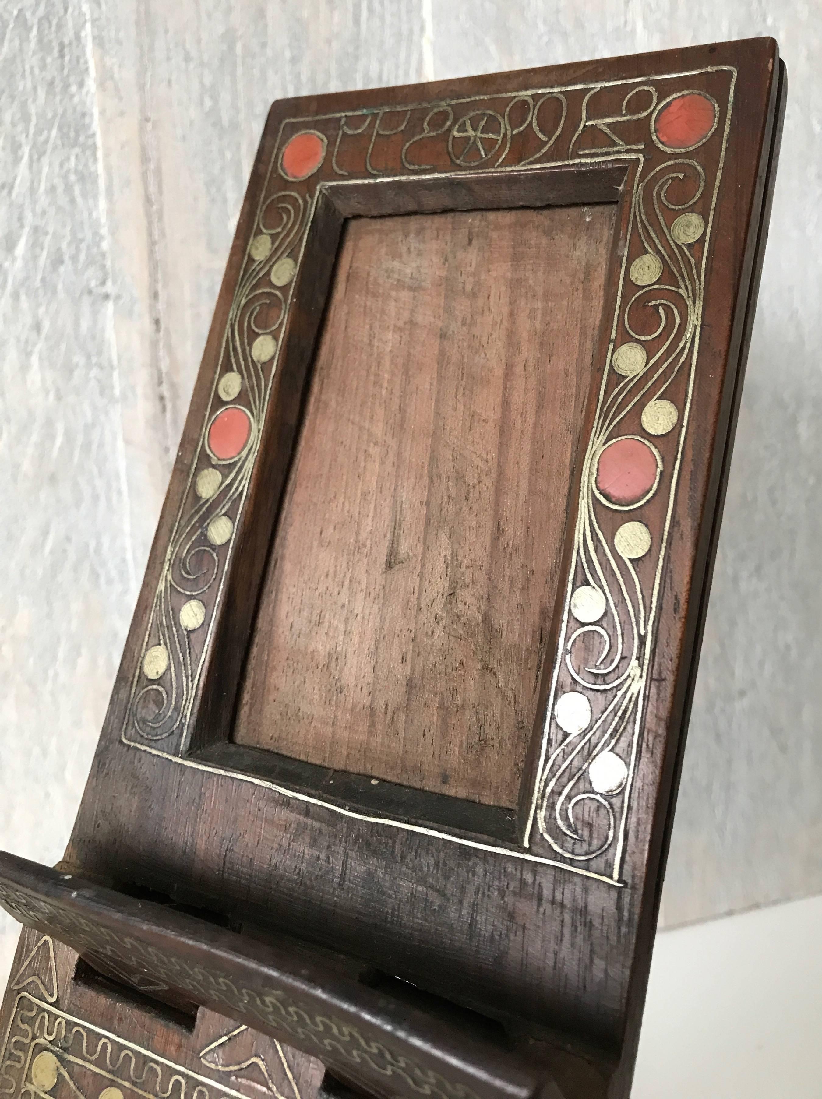 Handcrafted solid wooden, inlaid picture frame.

This, possibly Moorish, picture frame is easy to fold into a cross legged standing position and this rare example is inlaid with brass motifs and a glass-like red material. Thanks to its size it