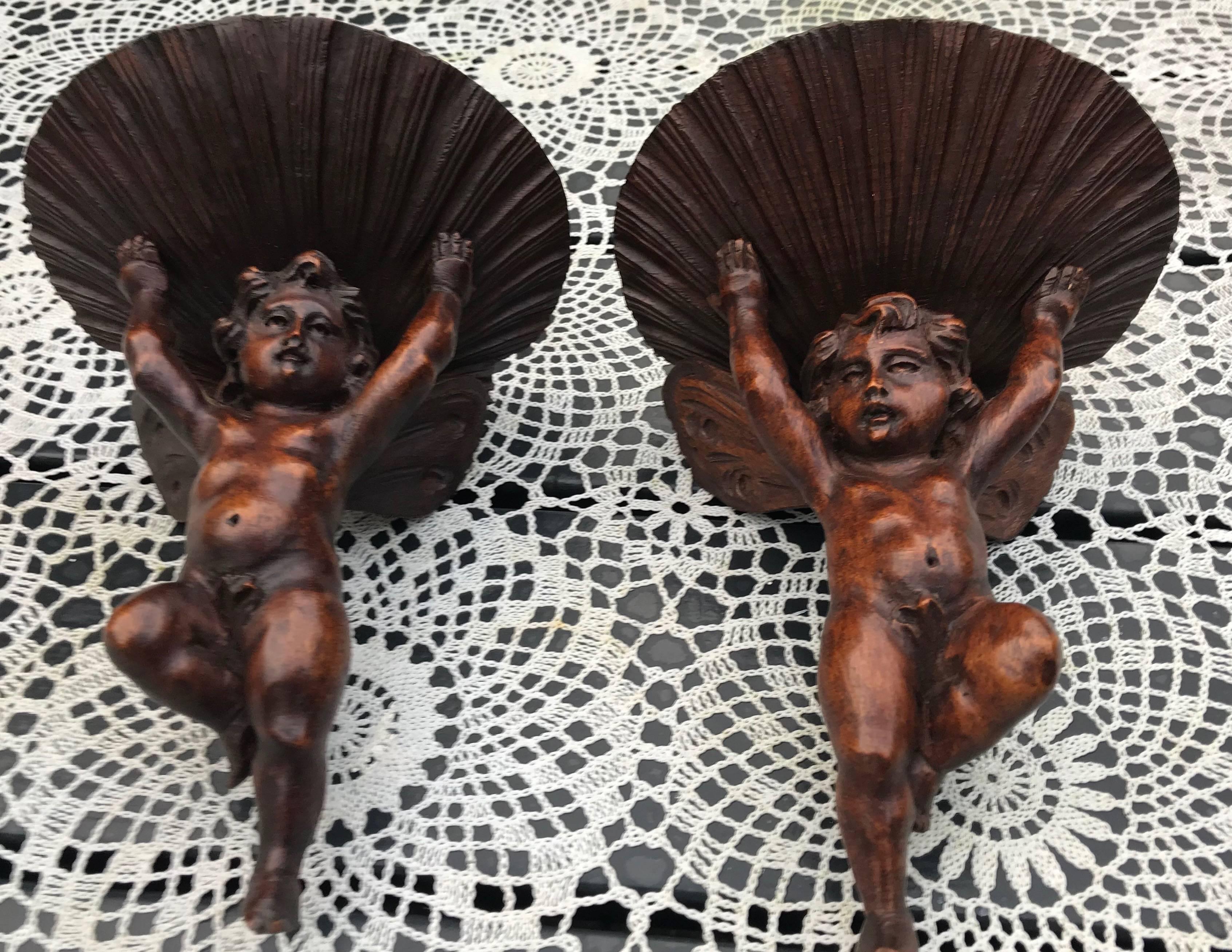 Rare and original pair of left and right mirrored wall brackets.

These antique wall brackets in the form of winged putti sculptures holding up shelves in the shape of shells are a real treat to collectors of the Baroque style. This quality carved