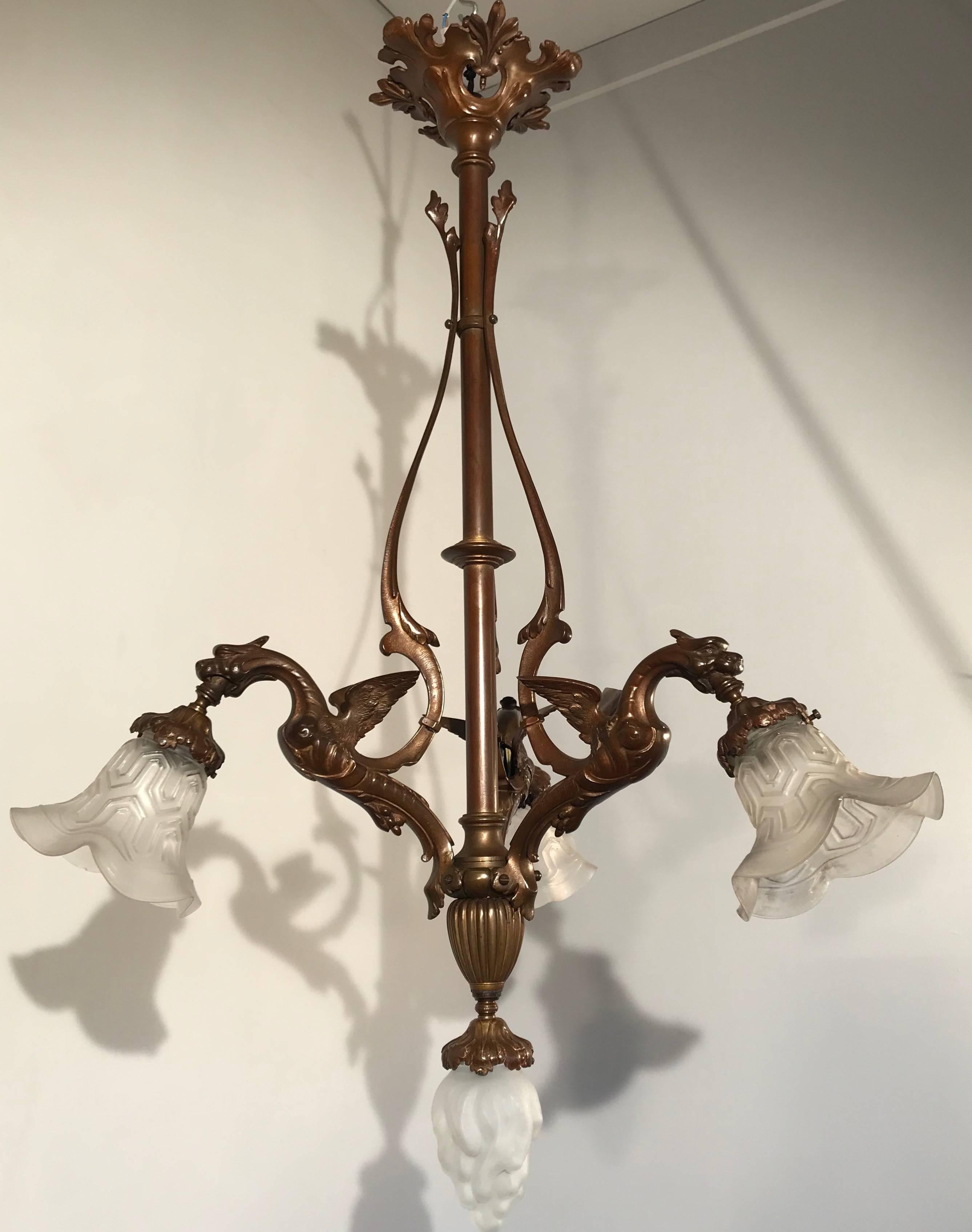 Striking early 1900s sculptural chandelier.

This antique and good quality chandelier comes with three beautifully crafted winged dragons. With the lamp shades in the position that they are, the light they radiate is like fire coming from the