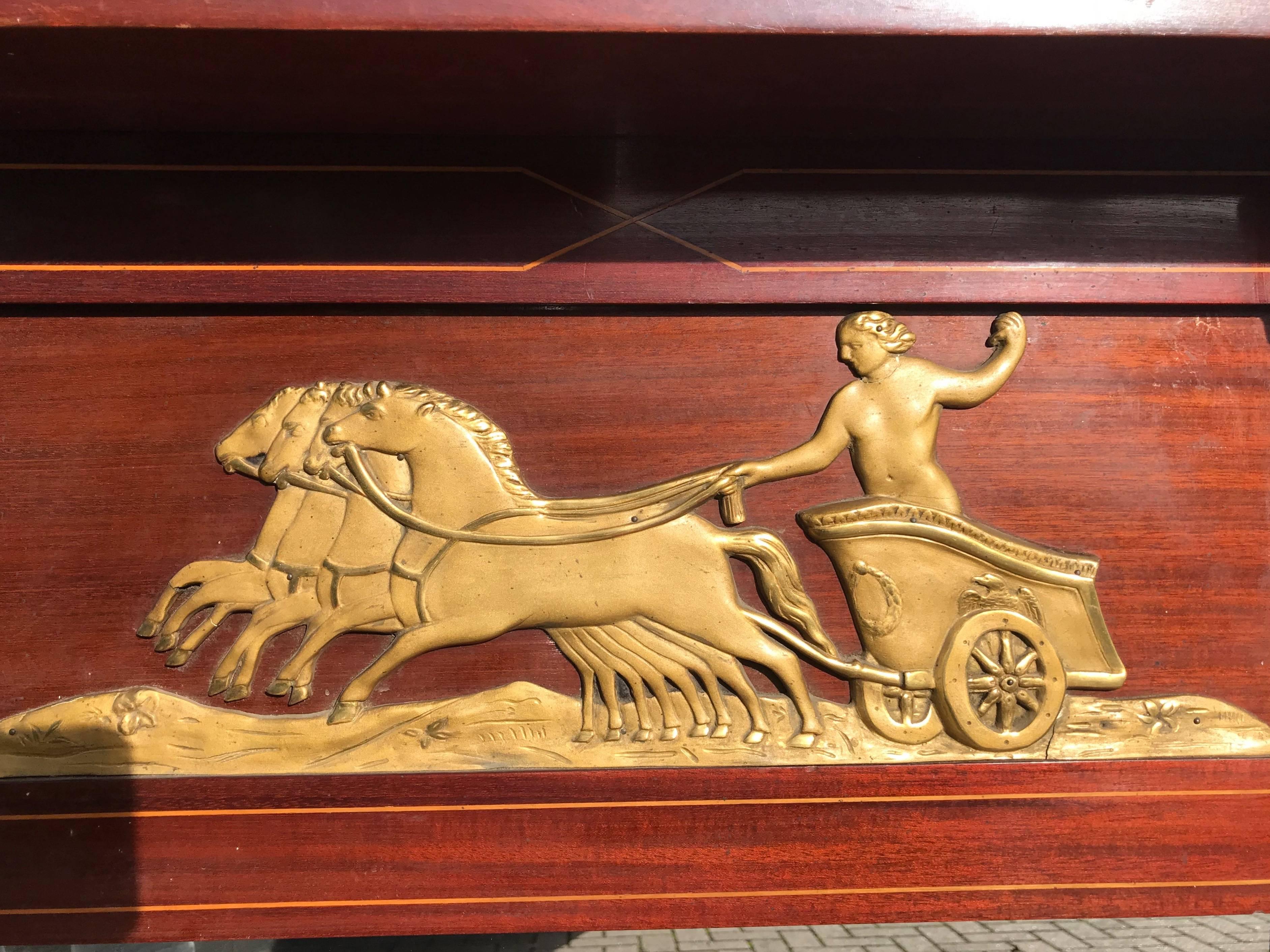 One of a kind, sizable and highly decorative mirror.
 
This stunning mahogany mirror frame is inlaid with a satinwood lining and decorated with a stylish and gilded chariot just below 'the roof'. For a cast plaster decor such as this four horse
