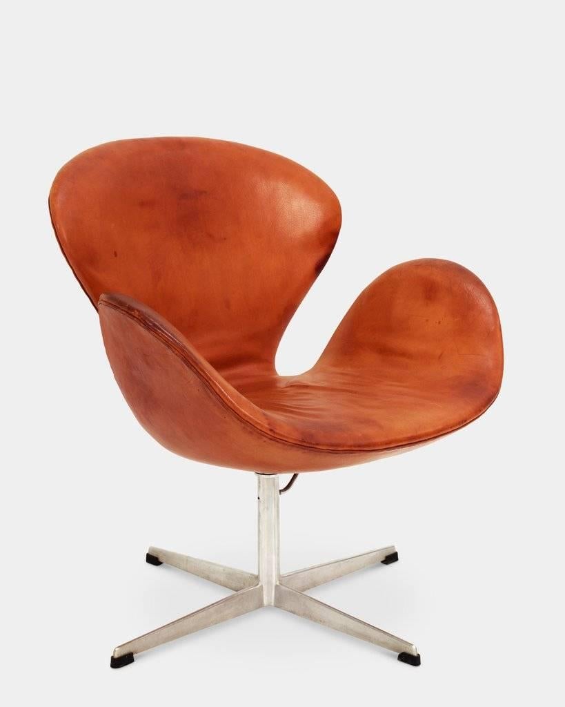 Arne Jacobsen (1902-1971):
 The Swan chair, model 3322. 
Armchair upholstered in original leather with patina, swivel four-star aluminium foot, heigh-adjustable stem. 
Originally designed in 1957-1958 for Hotel Royal in Copenhagen. 
Early model