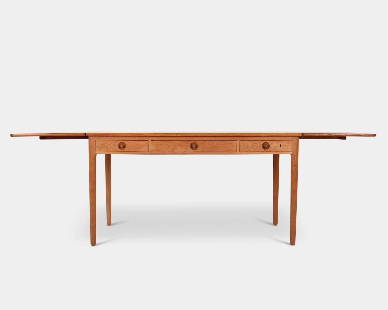 Hans J. Wegner (1914-2007):
Desk / Model AT-305
Oak desk with two drop-leaves, front with three drawers, one-drawer with pen compartment inside. Round tapered legs. Key included. 
Designed in 1955, manufactured and branded by Andreas