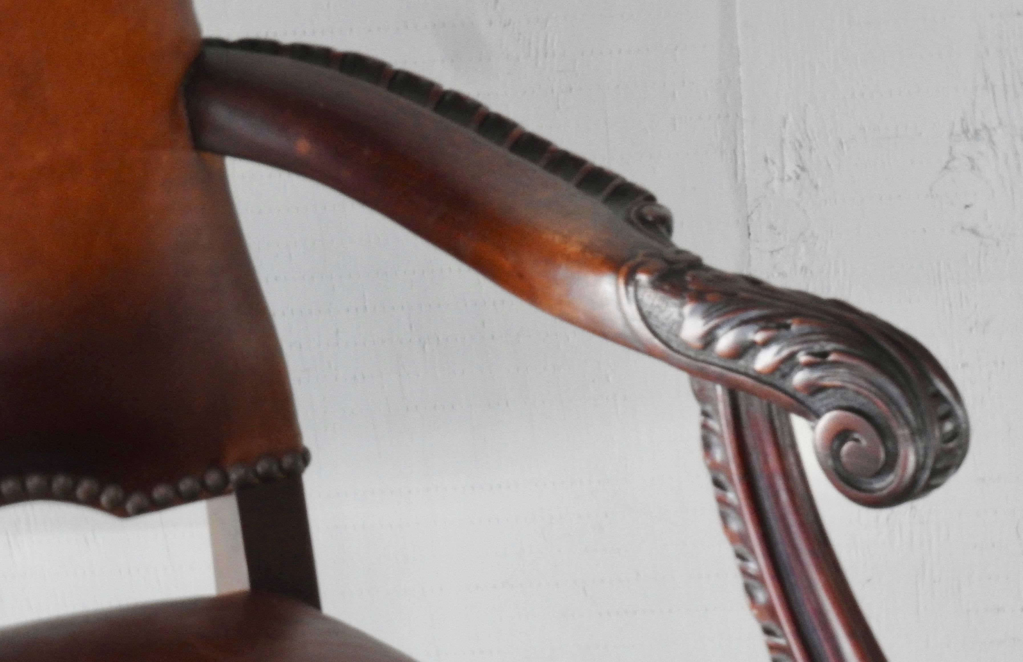 Carved walnut with leather make up this pair of 19th century American side chairs. Bronze tacks accent the edges. Hairy paw feet adorn the bottoms of the front legs and extend up to richly carved, curved legs. The arms form a graceful curve. The