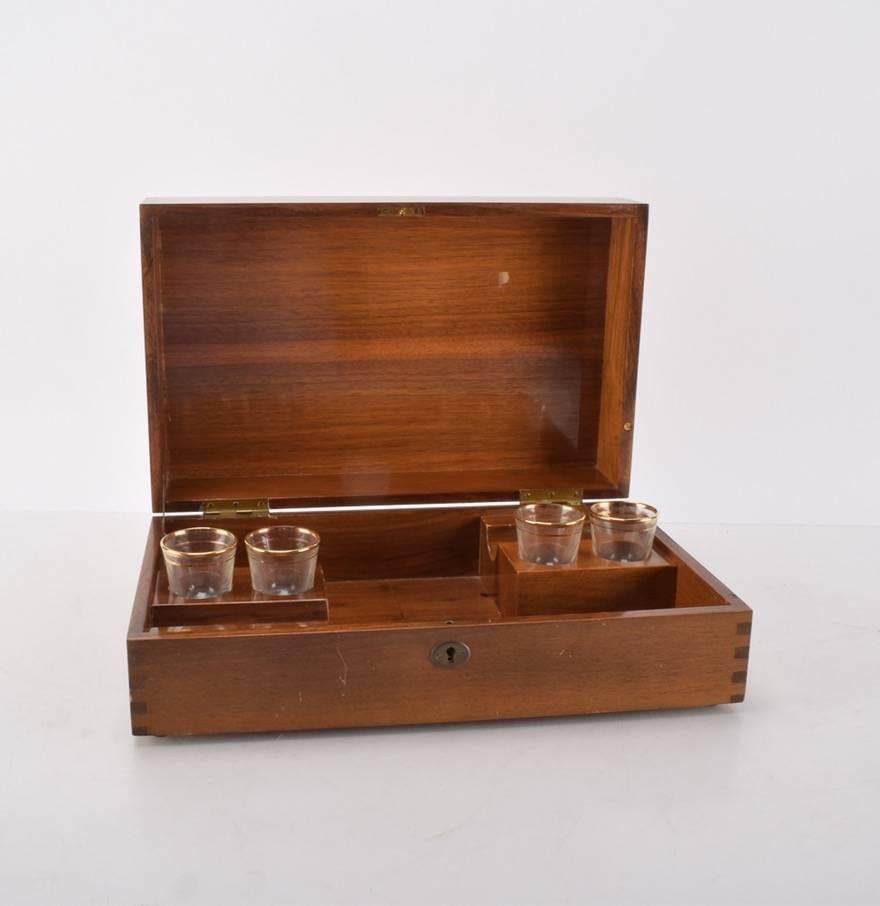 We are offering an elegant inlaid music box fitted to hold four shot glasses and two bottles. The exterior features dovetail construction, quartered veneer, and an inlaid oval with a horse’s head. The interior of the box has places to hold four