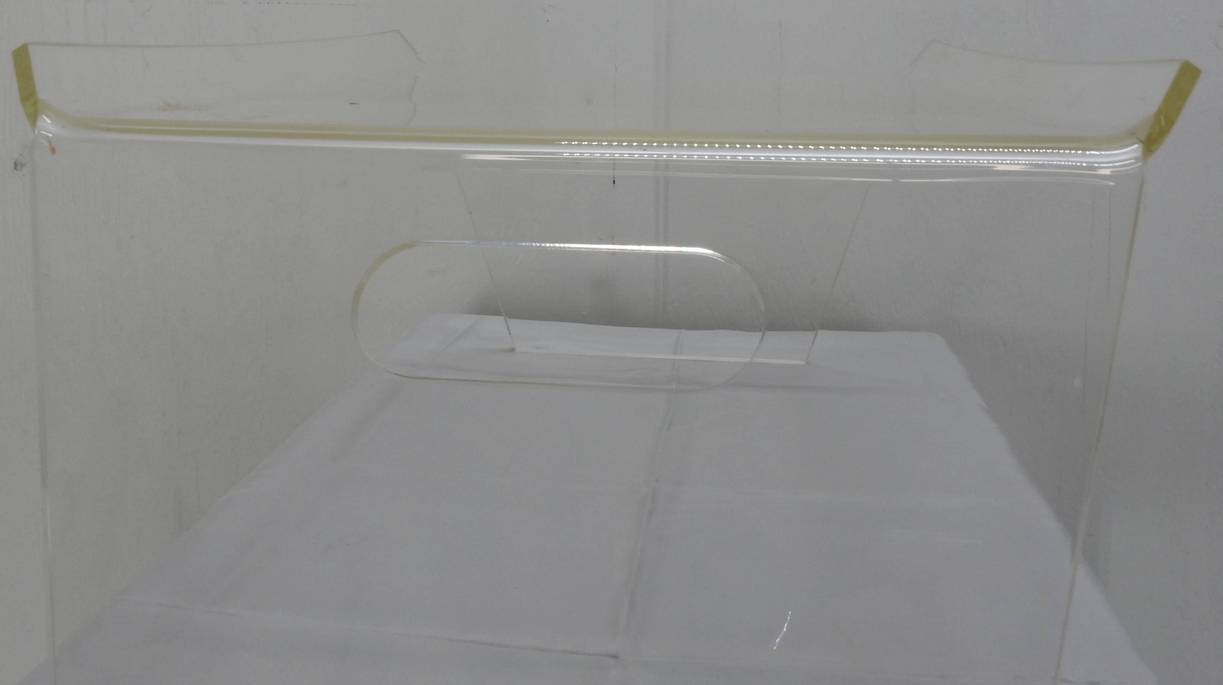 We are offering a clear Lucite bed tray. This tray has a rectangular surface with slanted rims along the long sides. It rests upon two splayed, trapezoidal legs with handle holes.
 