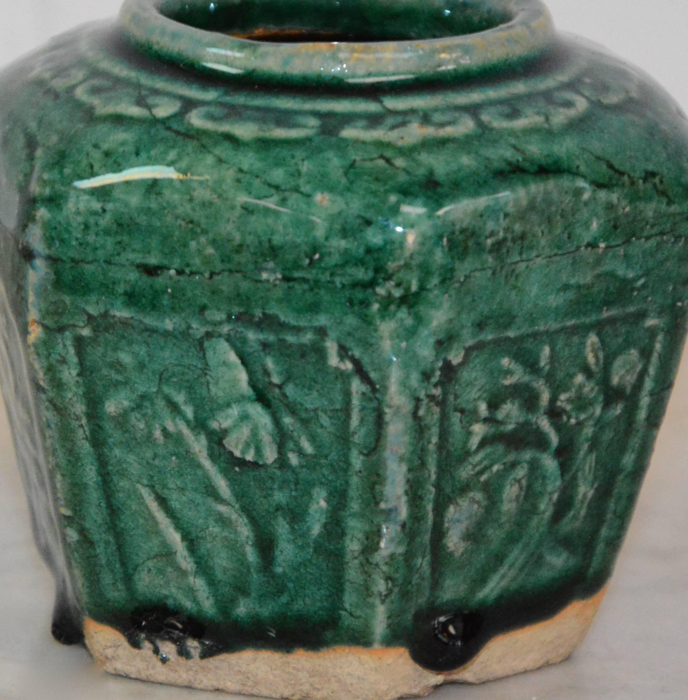 Featured is an antique Qing dynasty (1644-1911) ceramic wine vessel. This Chinese jar presents a round, faceted form with floral decorations in carved relief to each side and a decorative pattern encircling the mouth. It is glazed in jade green with
