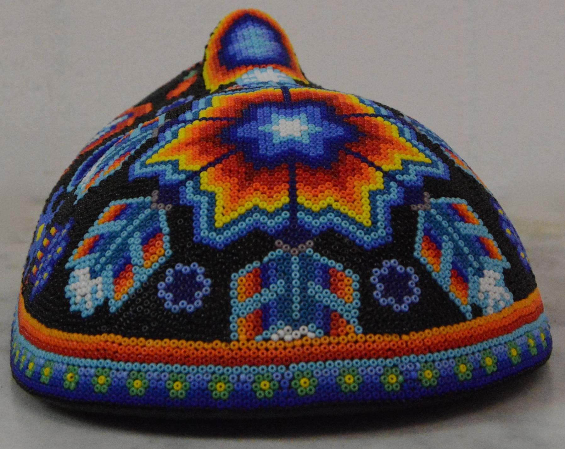 This is a colorful hand beaded Huichol Folk Art masks called Sacred Star Man. The mask features intricate tribal-like designs throughout that are comprised of glass beads in vibrant shades of red, orange, yellow, green, blue, purple, black, and