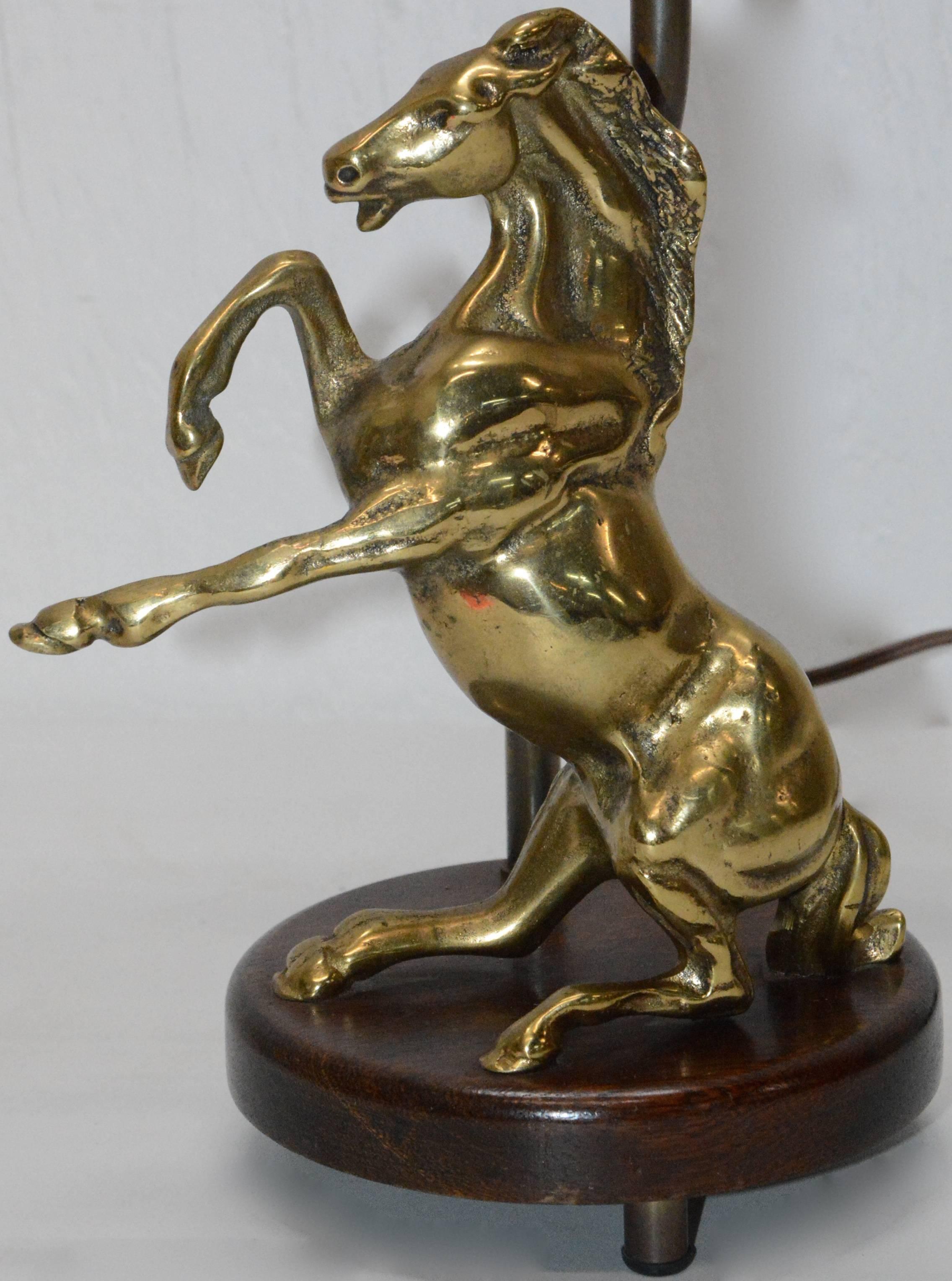 We are offering a vintage table lamp consisting of a round wooden base with a dark walnut stain. A polished, solid brass rearing horse sits atop the wooden base. The lamp is topped with a raw silk, brown colored shade with a hard lining and around